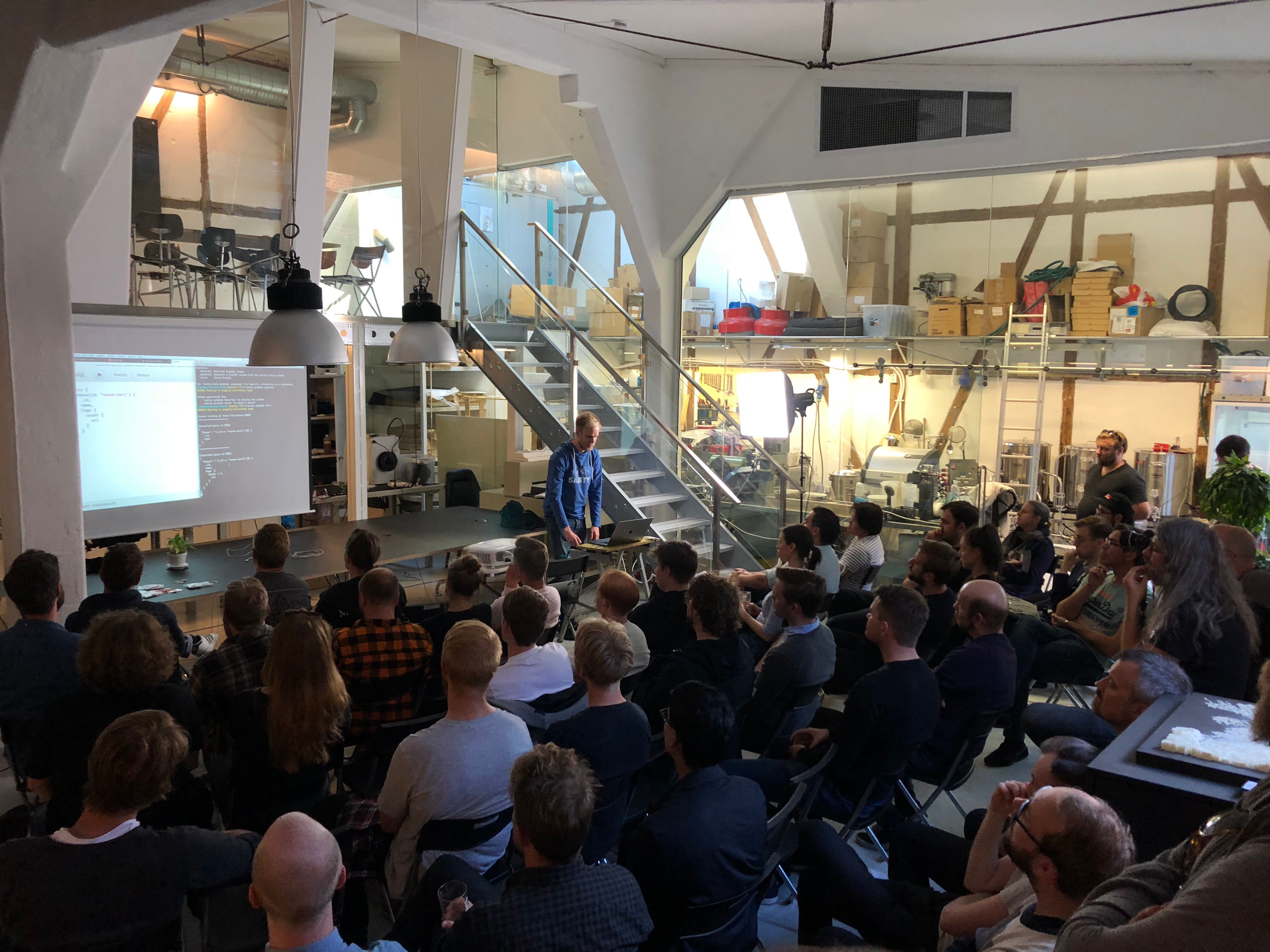 Espen presents code on a screen to a large audience in a modern industrial event space.