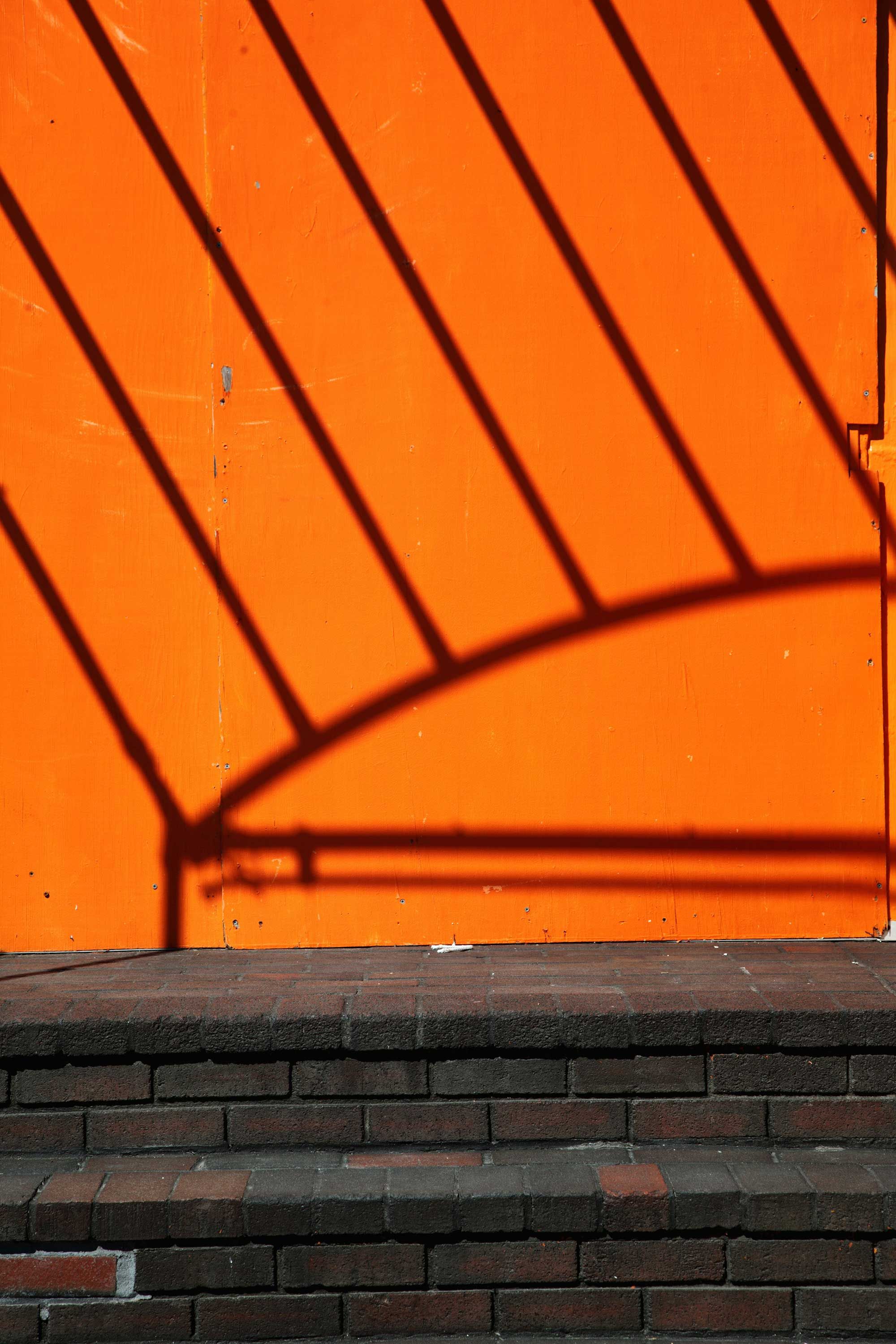 An orange wall with dark shadows of a railing, above a two-step brick staircase.