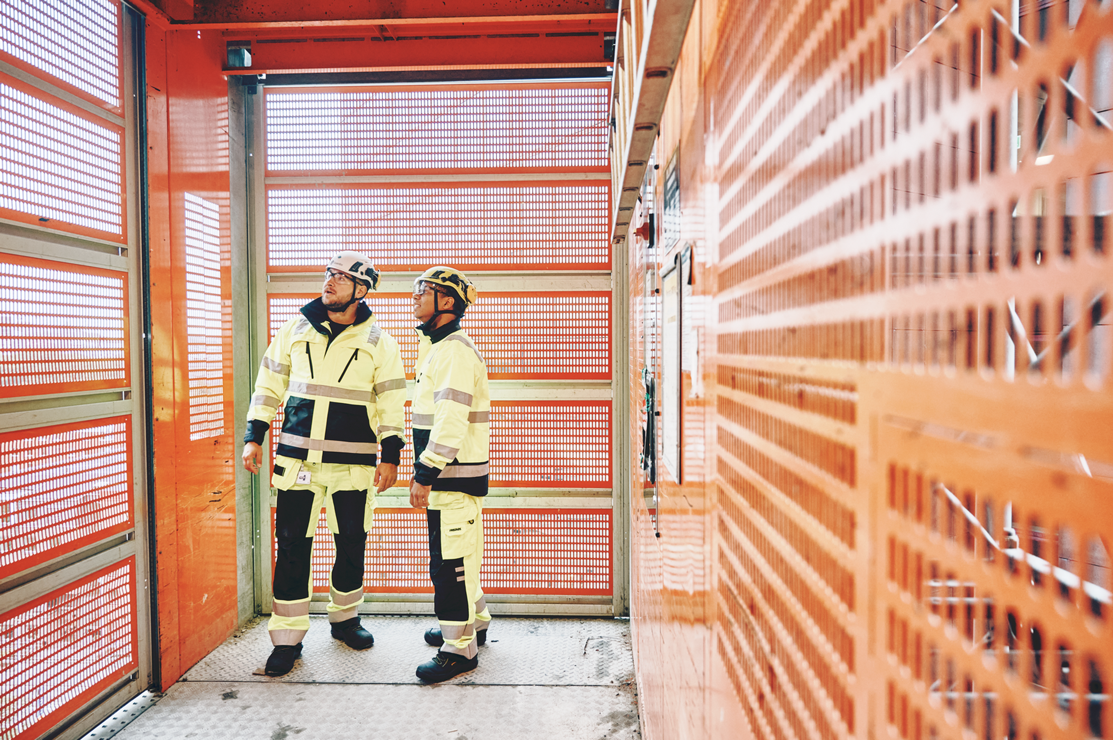 two construction workers are standing in front of an orange wall