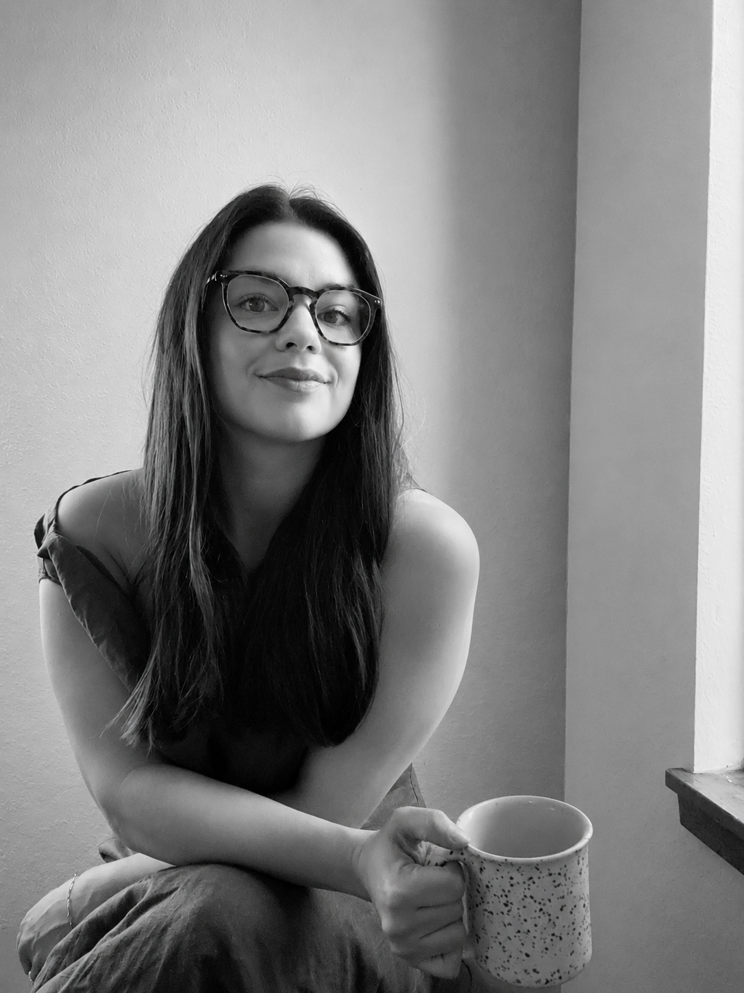 Black and white portrait of Monique Ritter, Enterprise Account Executive at Sanity, sitting near a window and holding a speckled mug.