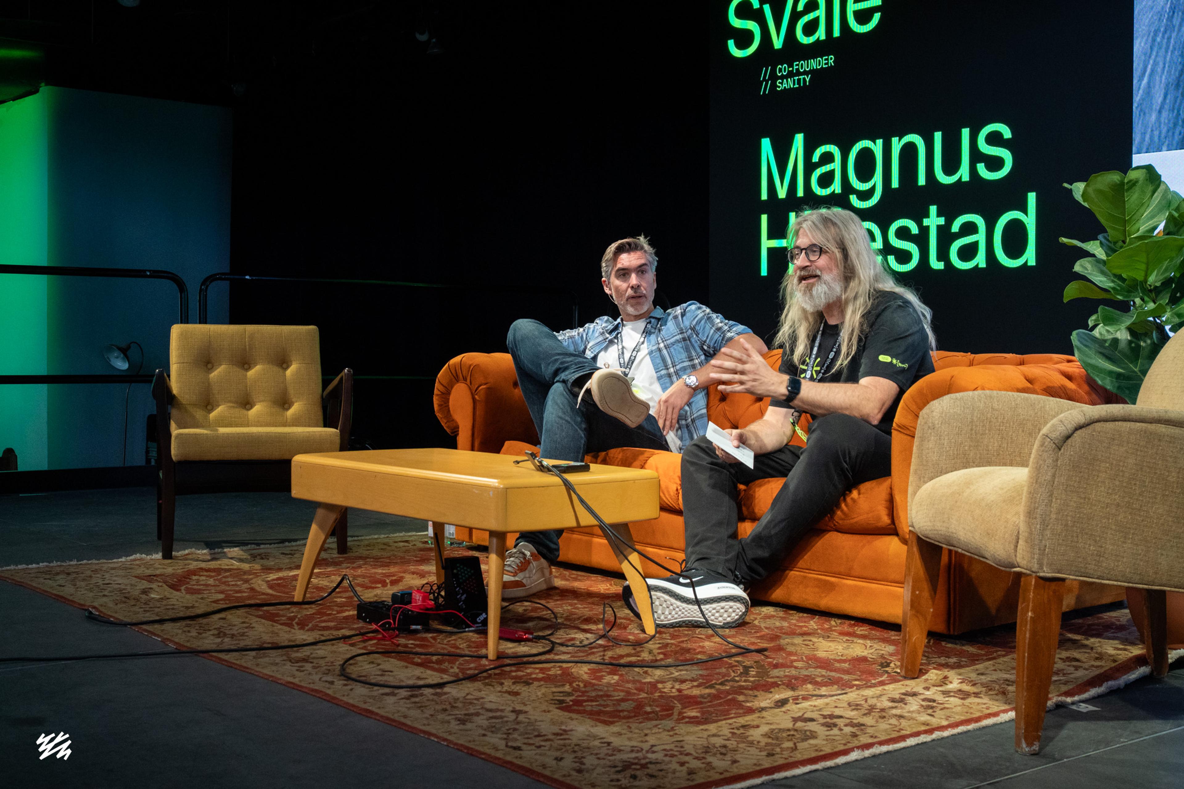 Magnus Hillestad and Simen Svale Skogsrud sitting on orange and tan sofas on stage at Everything NYC, having a conversation. Screen behind them displays their names in green text identifying them as Sanity co-founders. Yellow coffee table in foreground with microphones.