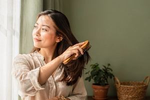 Una donna si spazzola i capelli davanti alla finestra.