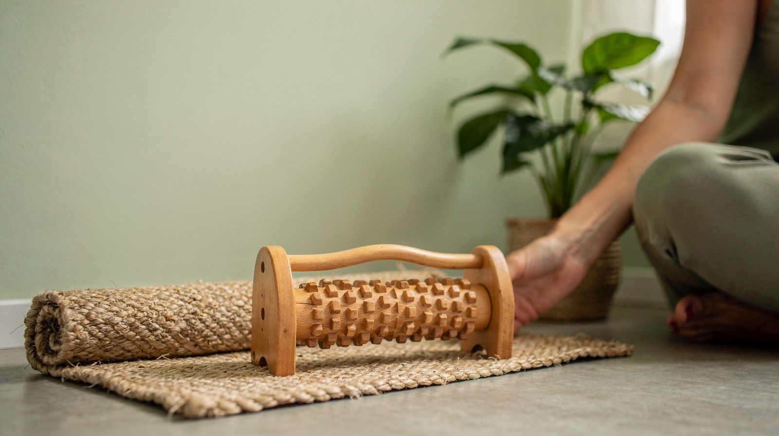 Un rullo di legno per i piedi e un tappetino arrotolato accanto a una pianta.
