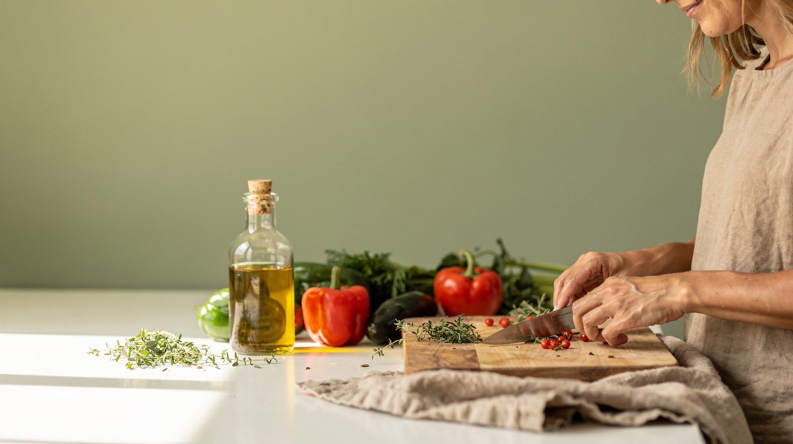 Il piano di una cucina luminosa con verdure, olio ed erbe pronti da usare.