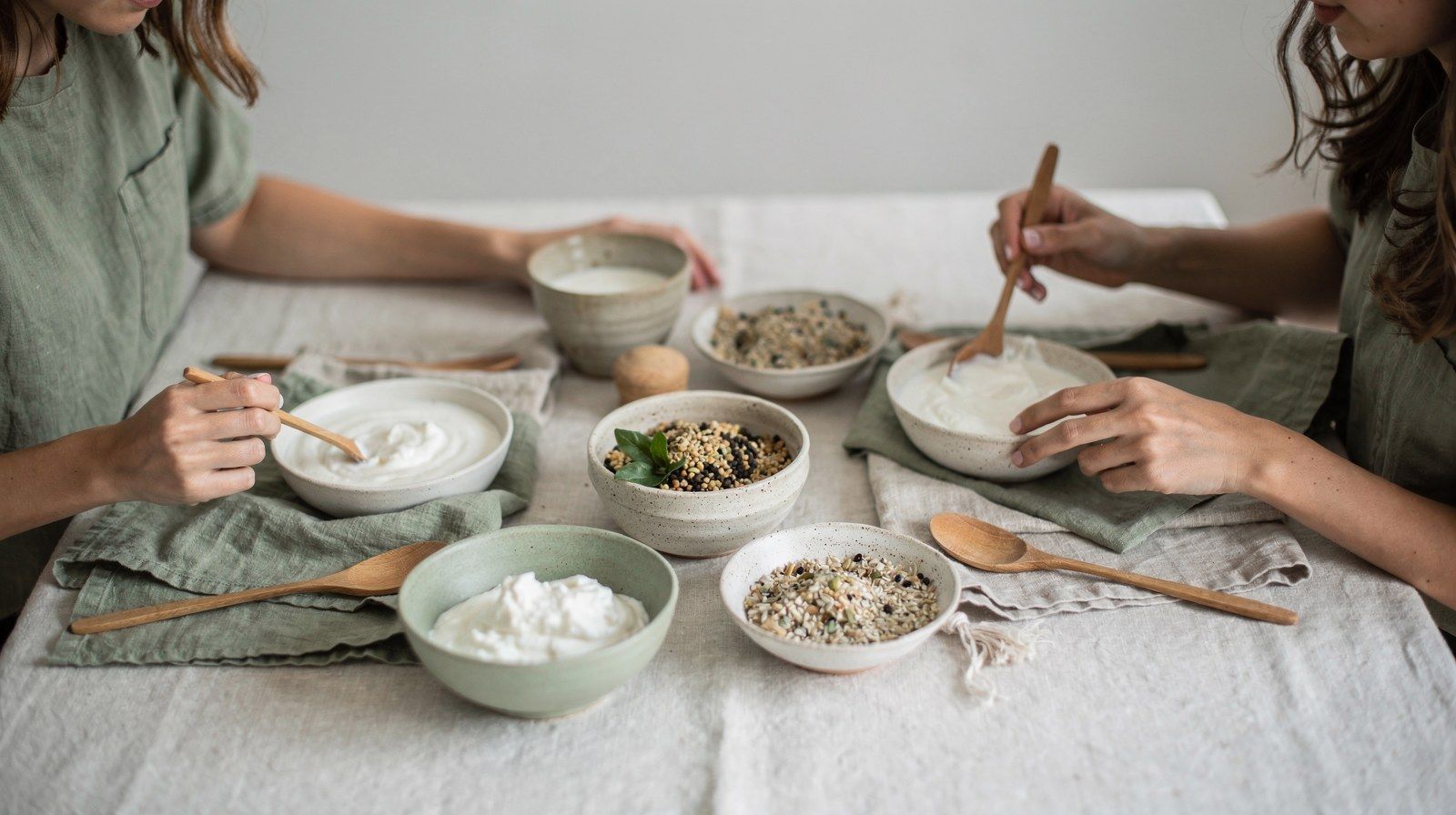 Piccole ciotole di yogurt, kefir e cereali su un tavolo chiaro, viste dall’alto.