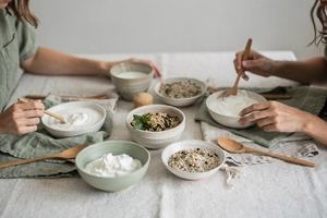 Piccole ciotole di yogurt, kefir e cereali su un tavolo chiaro, viste dall’alto.