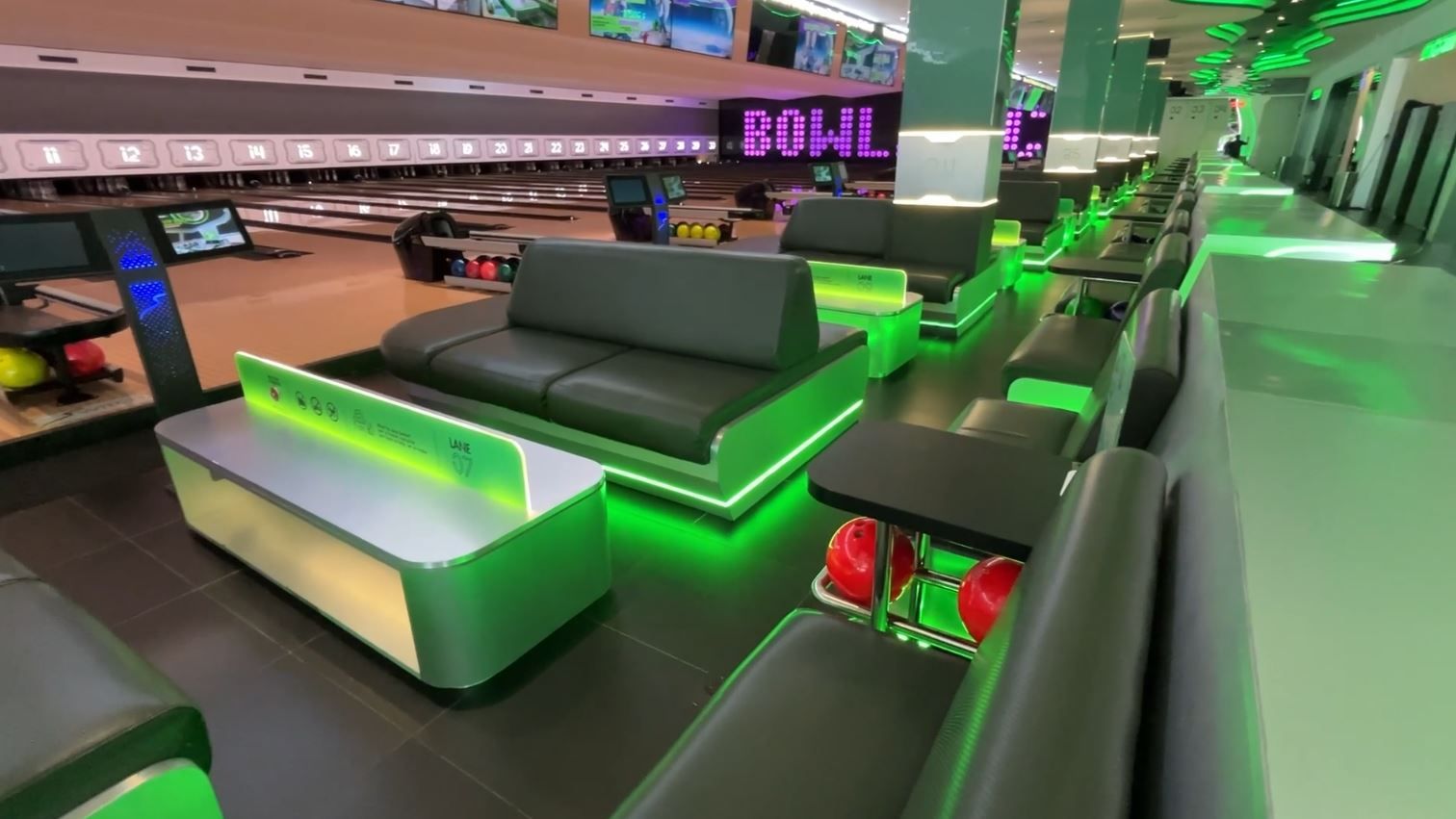 Sofa berlapis abu-abu dan area duduk dengan pencahayaan hijau di sisi lintasan Bowl.inc