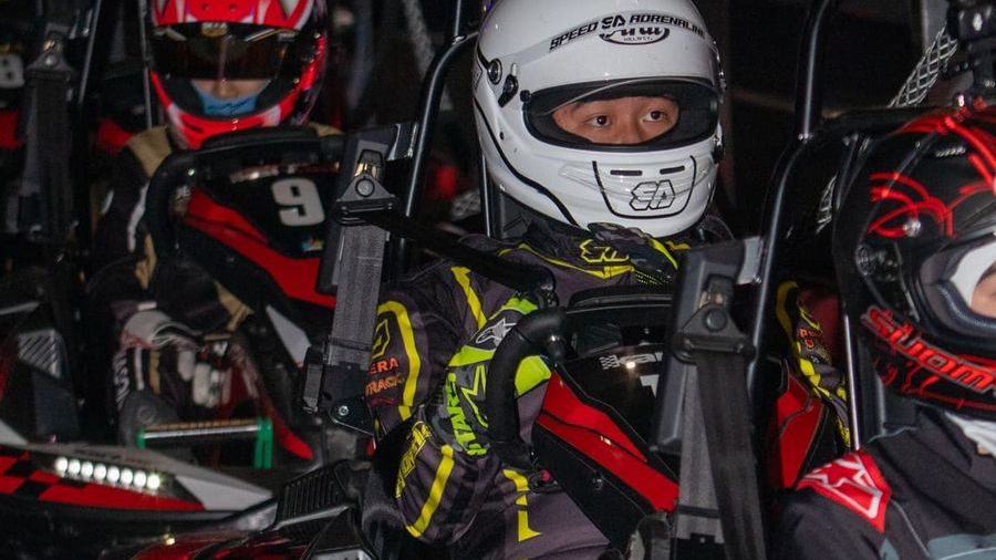 Pembalap Kart.inc mengenakan helm, balaclava, sarung tangan, dan seragam tim di atas gokart