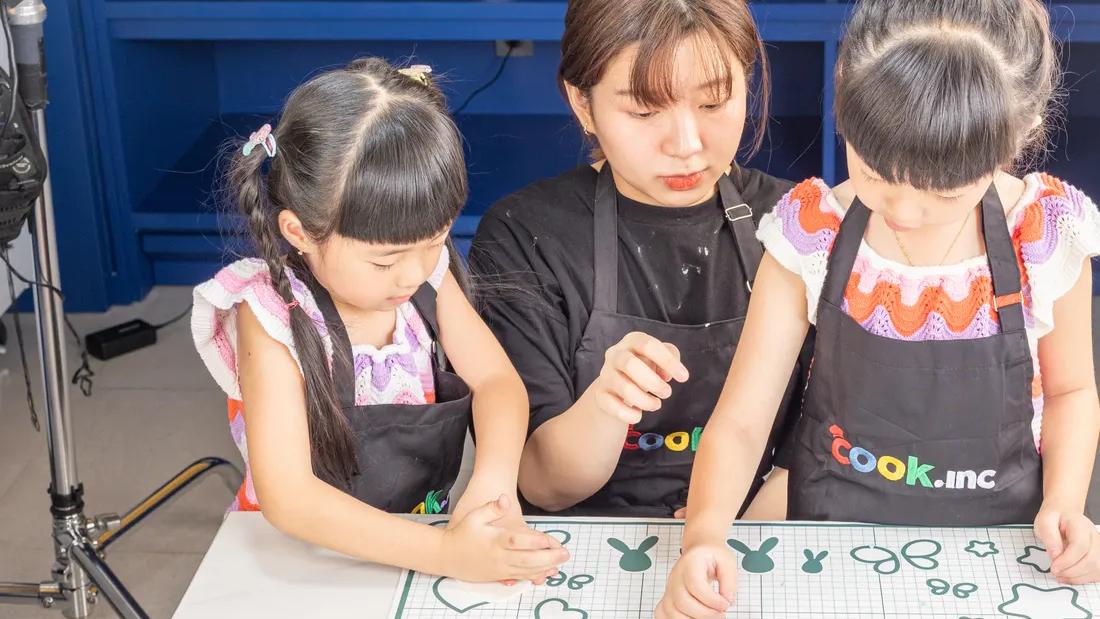 Dua anak mengikuti kelas memasak Cook.inc bersama pendamping di meja kerja ramah anak