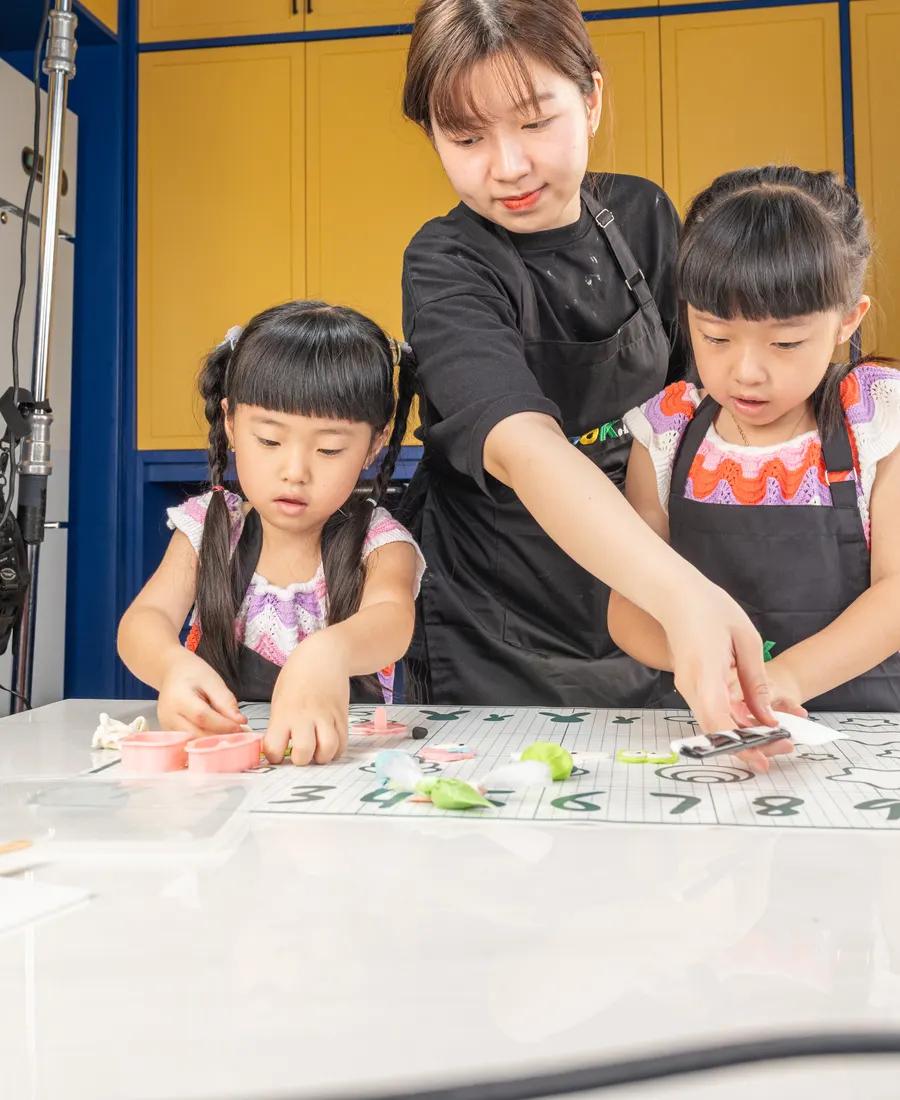 Dua anak mengikuti arahan chef di meja kerja Cook.inc