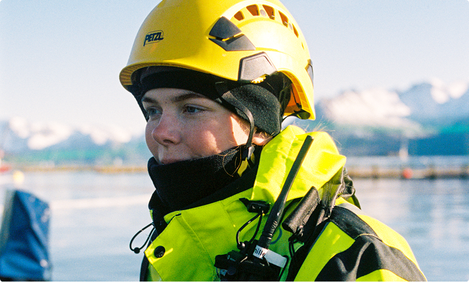 A farmhand in a yellow helmet on the walkway of a salmon pen