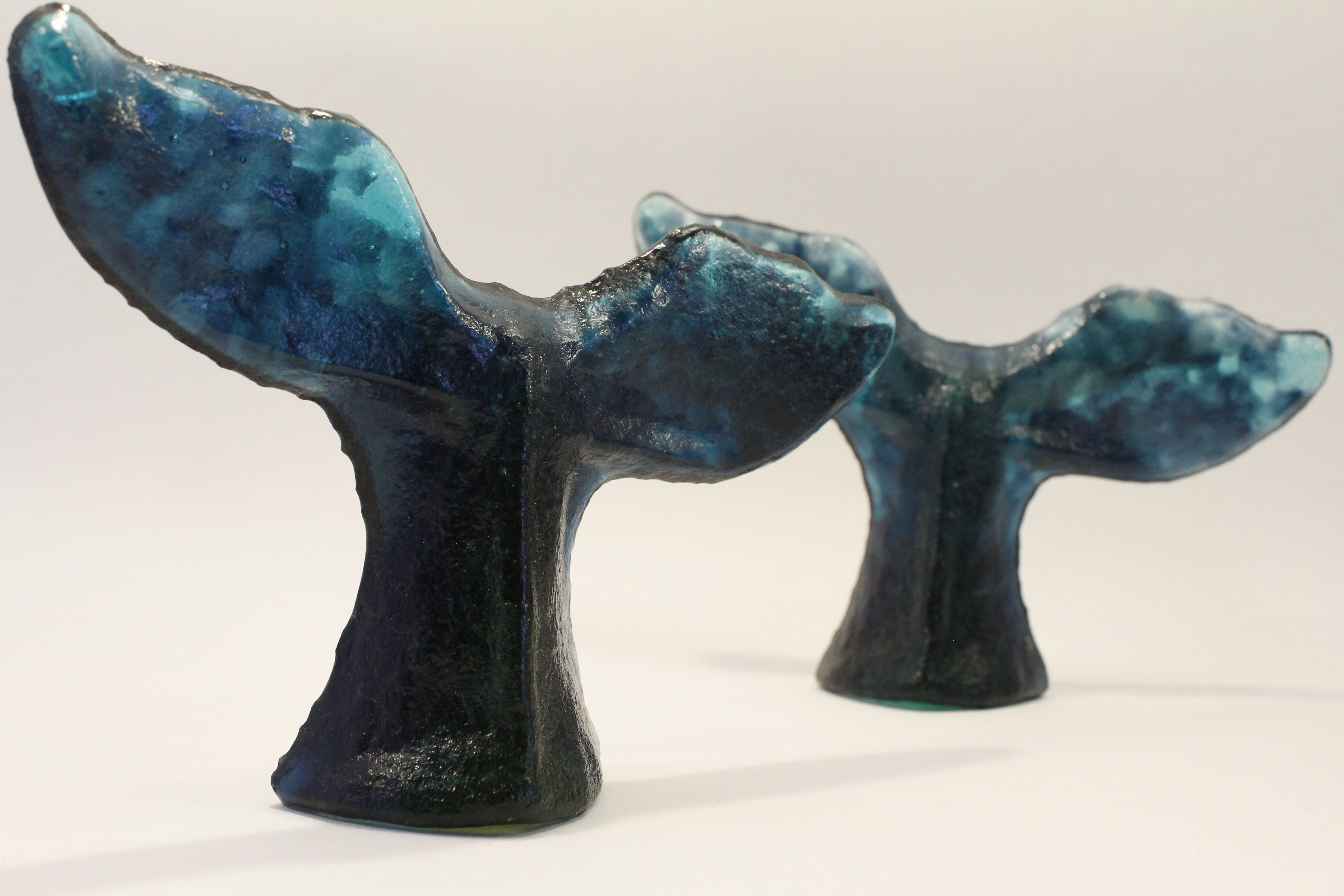 Two blue glass sculptures shaped like whale tails