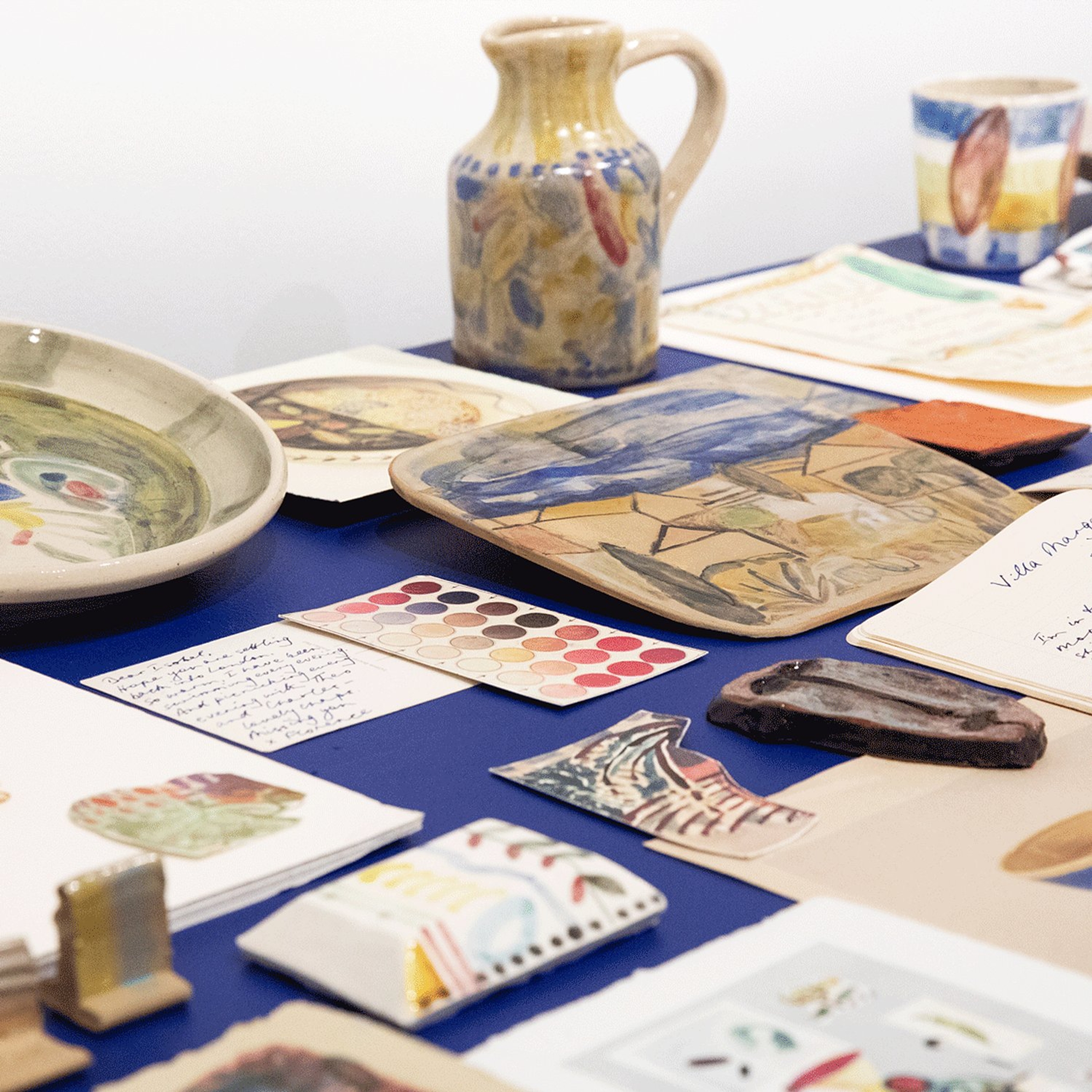 Julia Holderness’ Villa Margaux: a studio archive, a table laid with painted ceramics, jugs and handwritten papers.