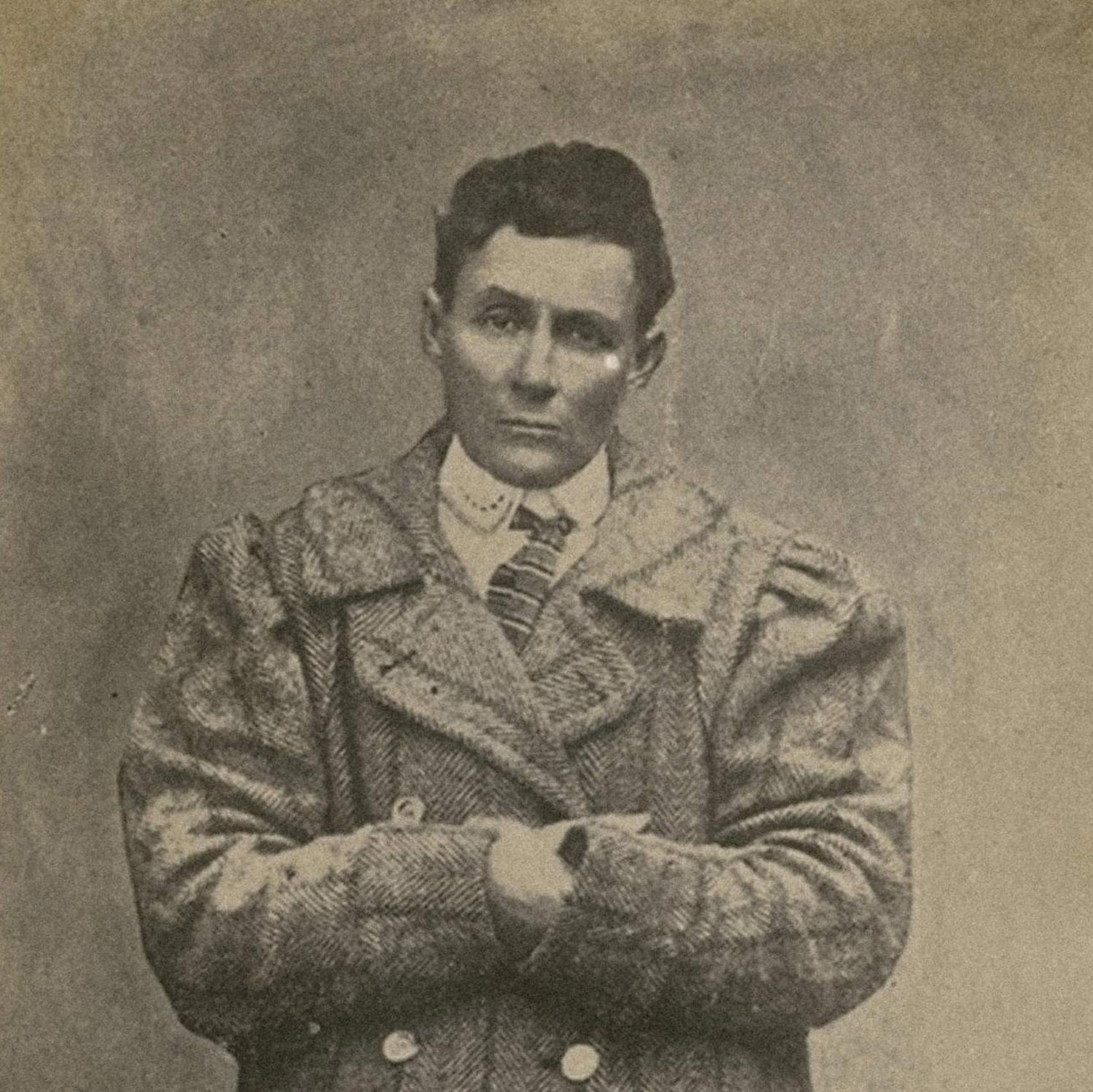 Postcard portrait of Amy Bock dressed in men’s clothing, standing in a long overcoat with a high collar.