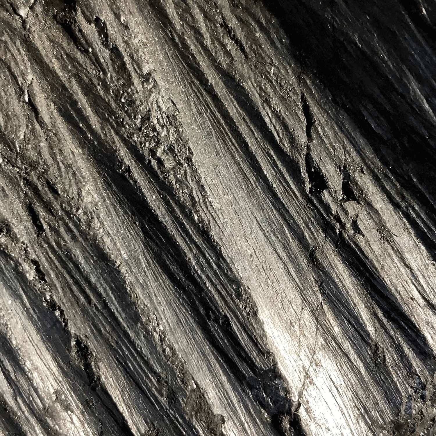 Video still of a dark, glinting coal face with deep diagonal ridges.