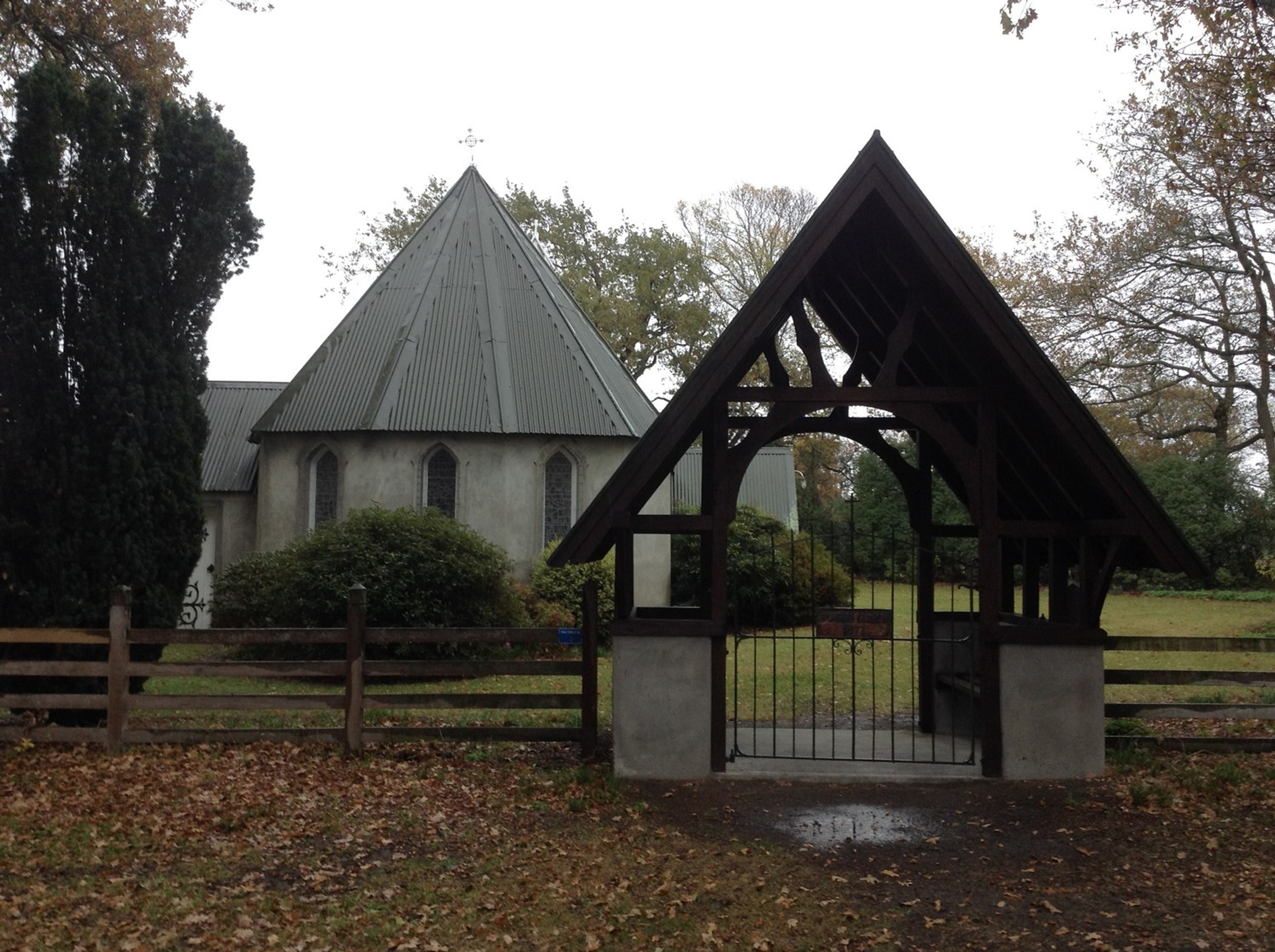 The small Church of St John the Evangelist at Barrhill, seen through a wooden lychgate among trees.