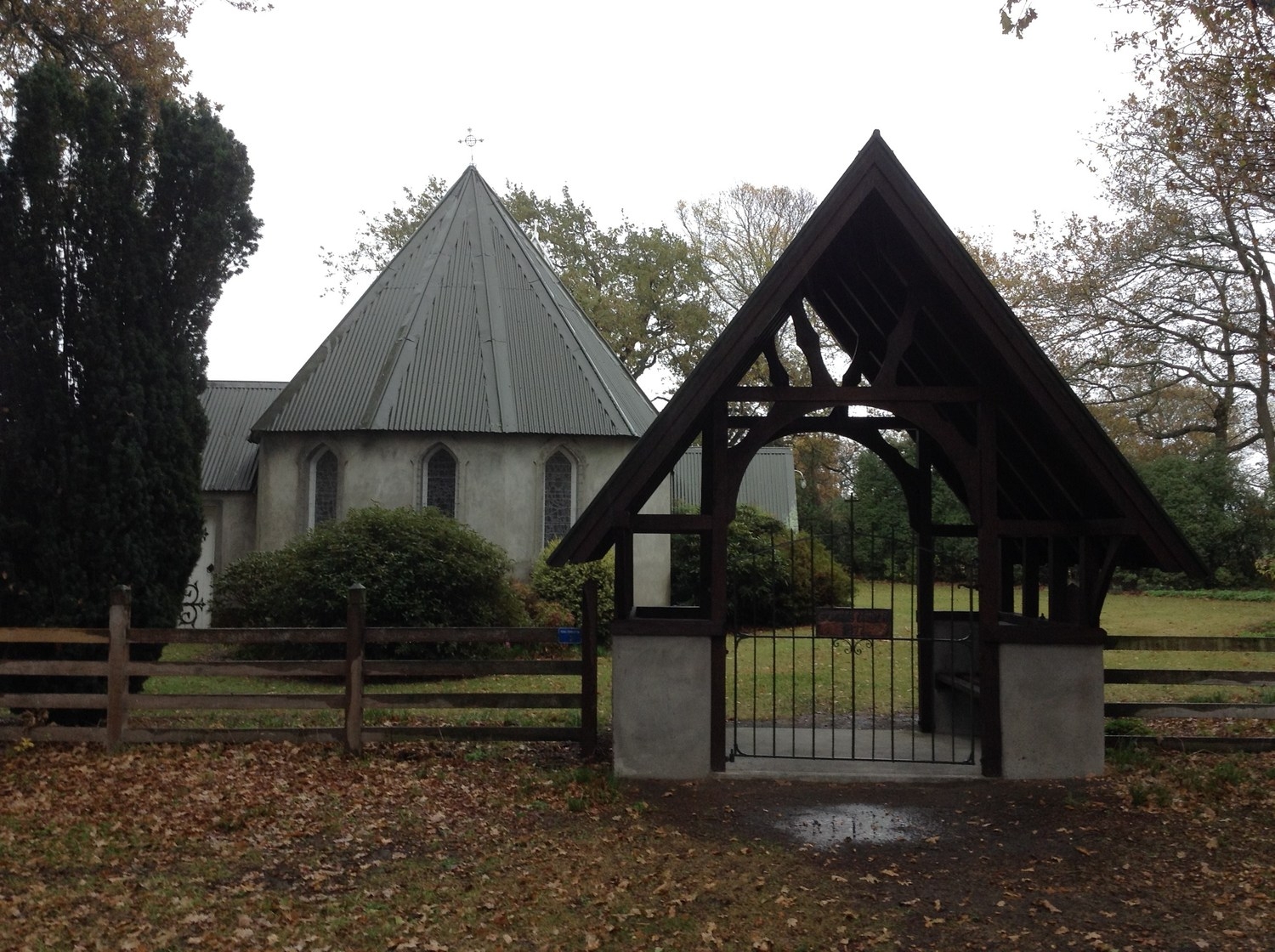 The small Church of St John the Evangelist at Barrhill, seen through a wooden lychgate among trees.
