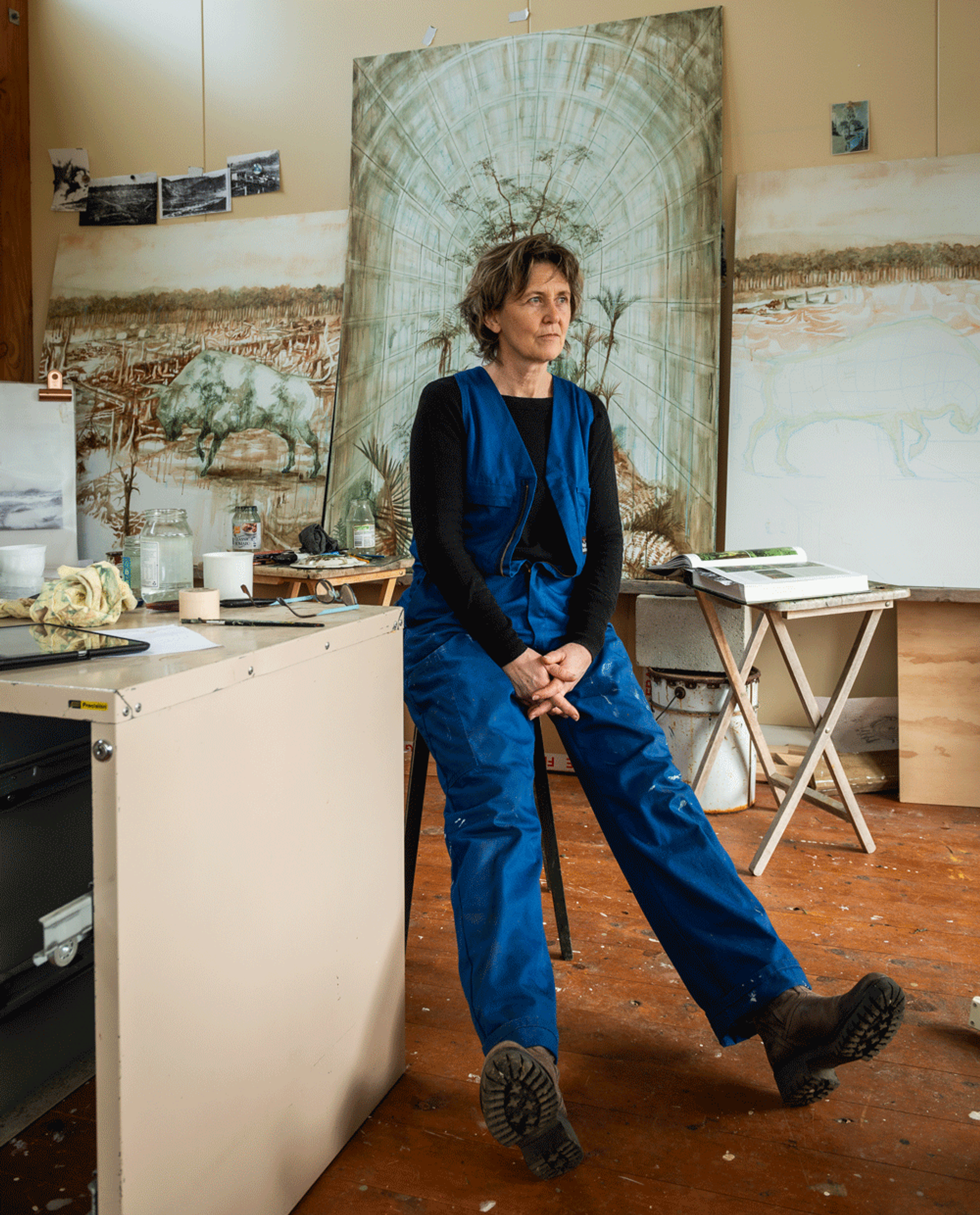 Jenna Packer sitting in her studio, with works in progress on the wall behind her.