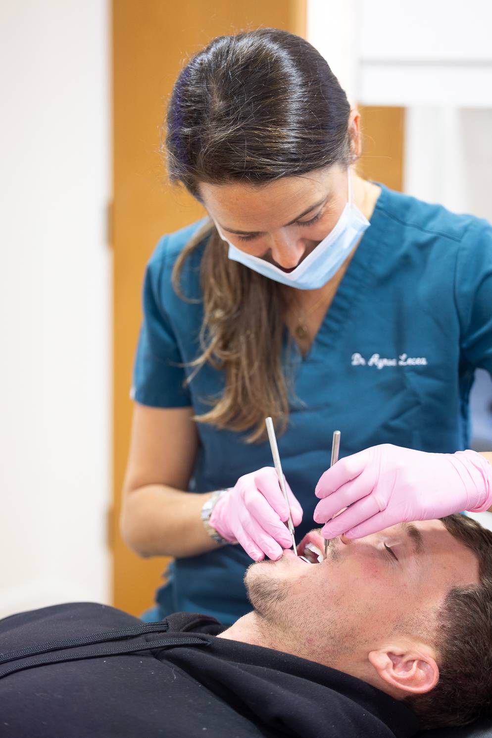 A dentist wearing a face mask inspects a patient's teeth