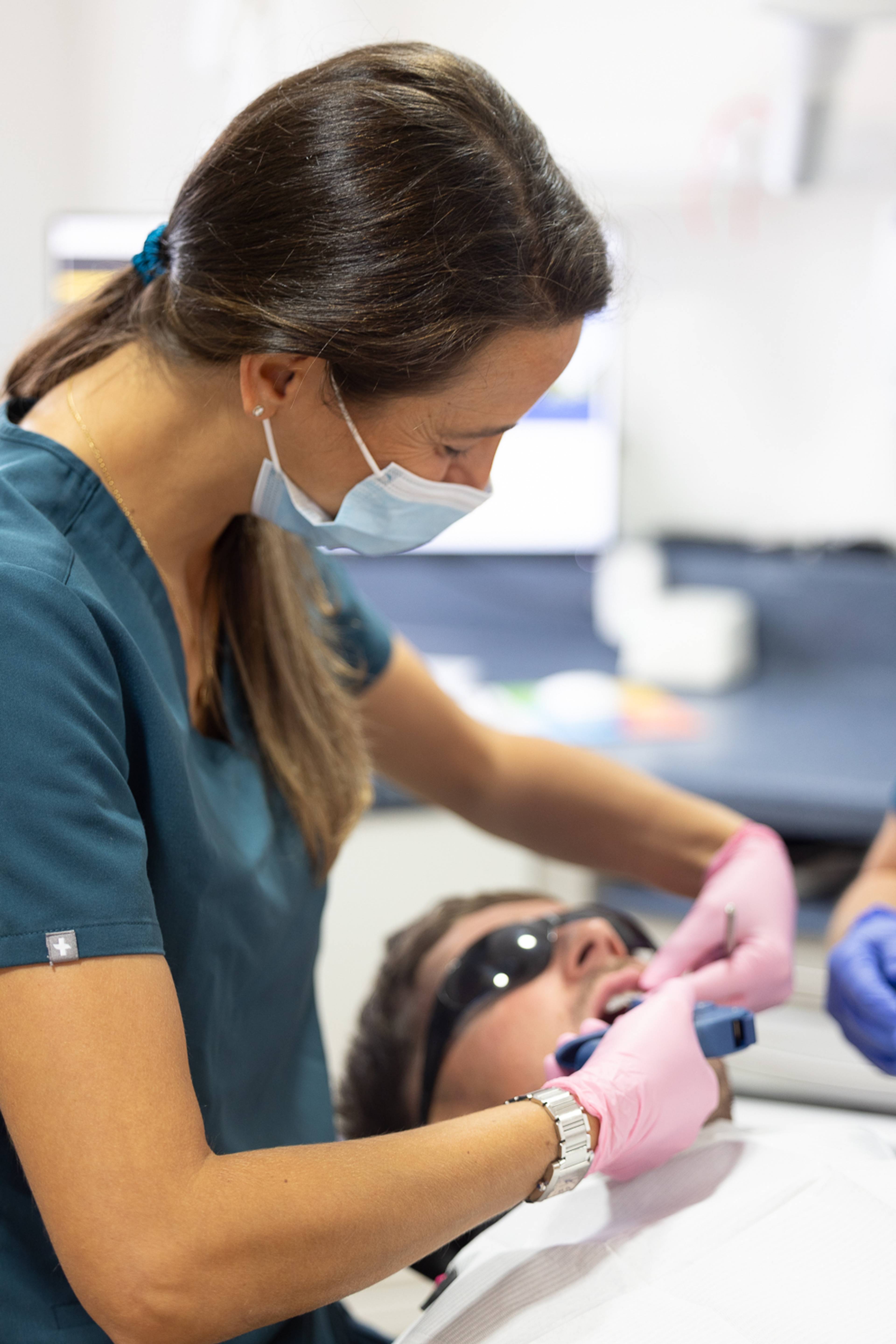 A dentist wearing a face mask works on a patient who is wearing eye protection