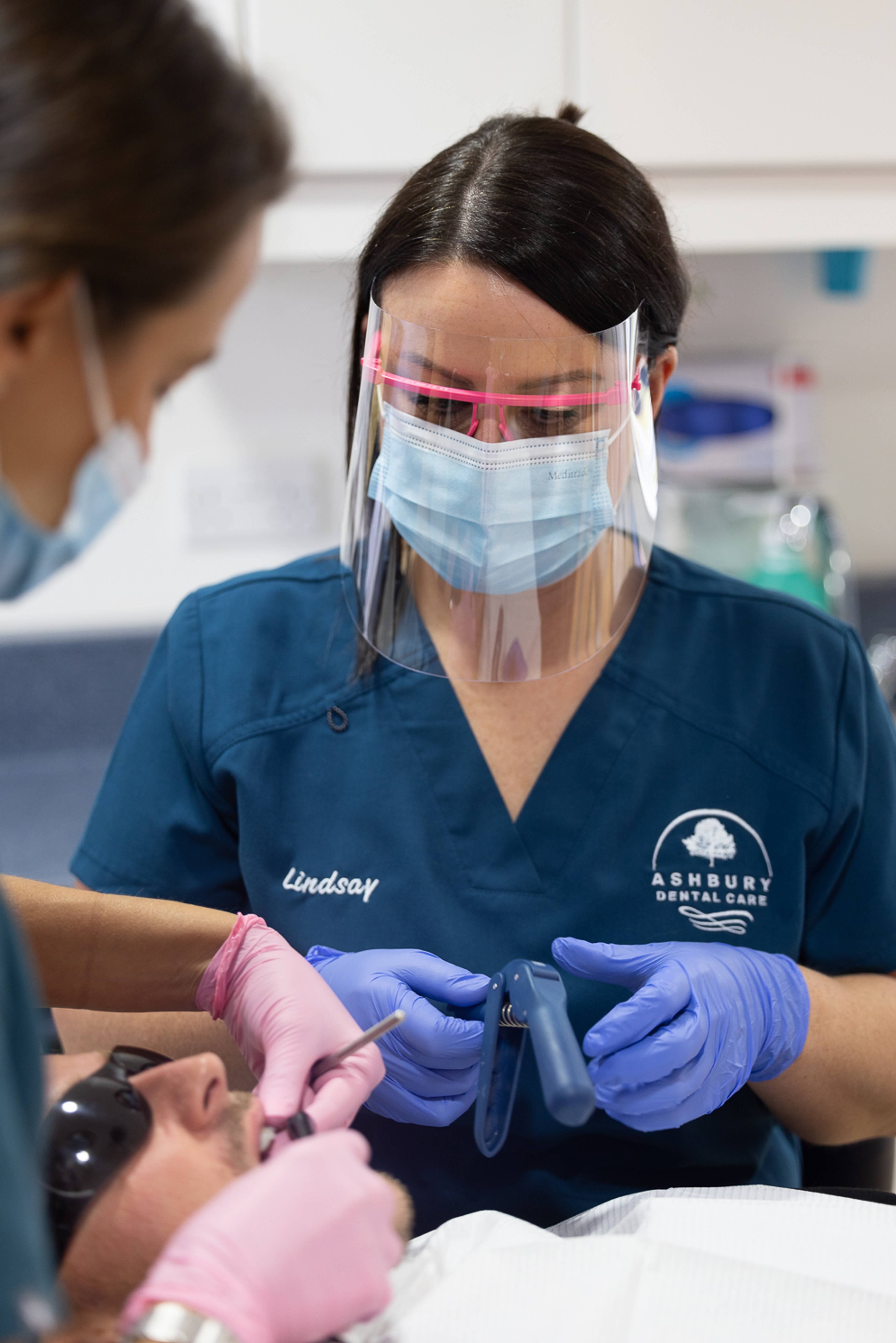 Two dentists work on a patient who is wearing eye protection