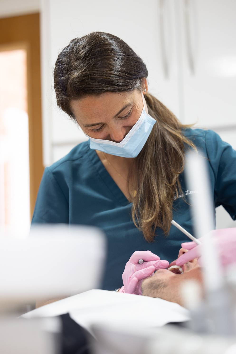 A dentist wearing a face mask inspects a patient's teeth