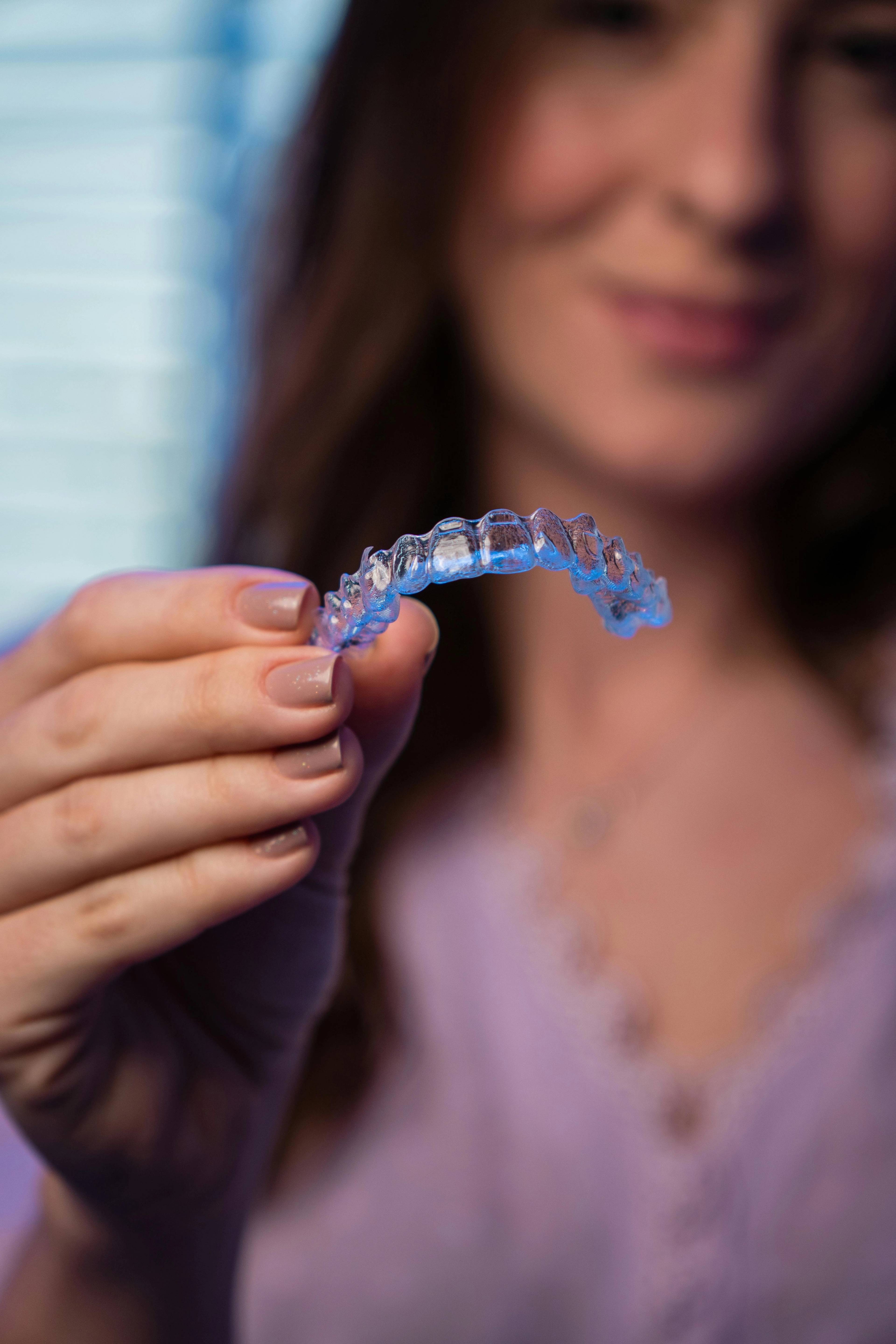 Patient holding a clear aligner highlighted with a blue light