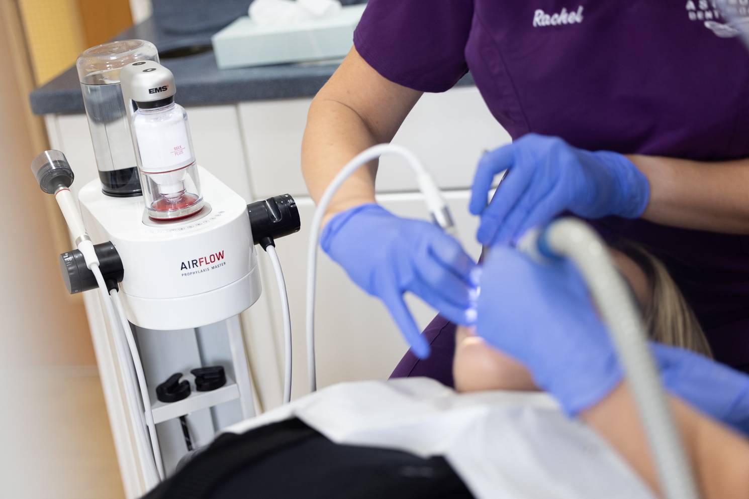 A dentist using an airflow tooth cleaning machine on a patient