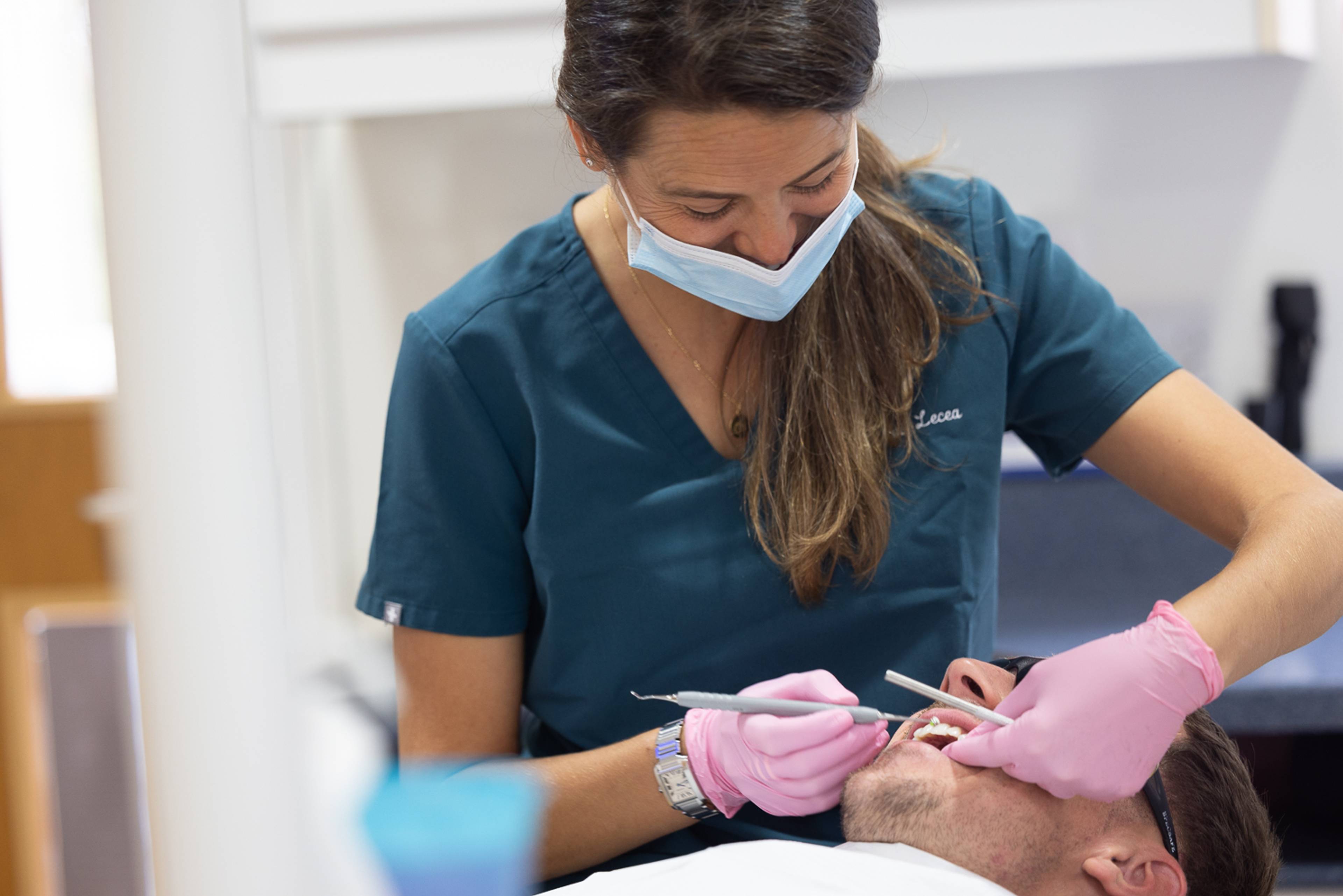 A dentist wearing a face mask and pink latex gloves works on a patient's teeth using some dental tools