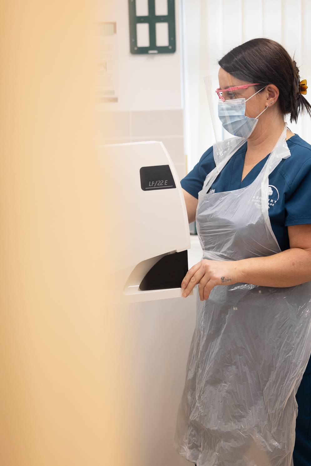 A dentist in a face mask calibrates a machine that is out of frame