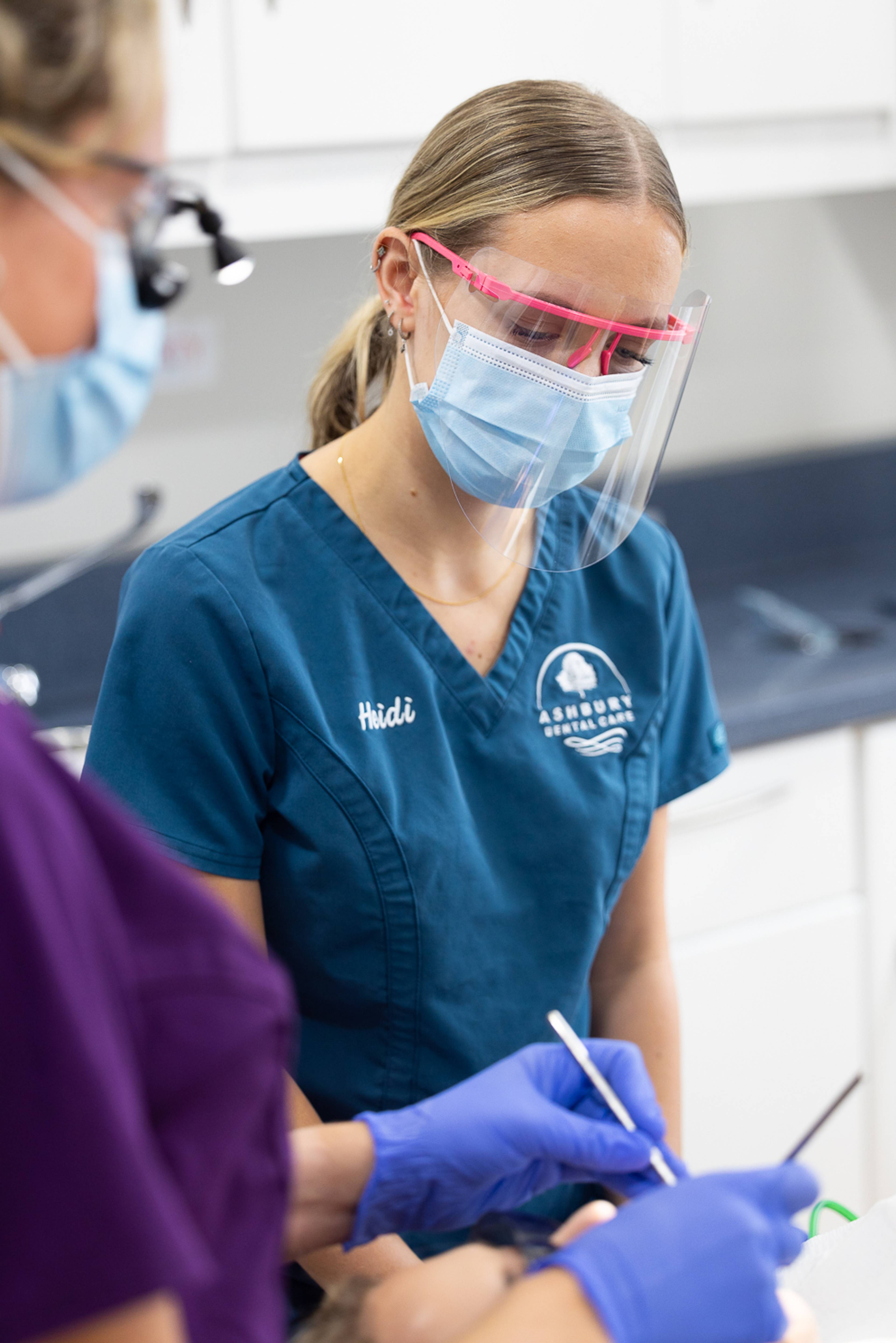 Two members of dental staff at Ashbury Dental Care in their branded scrubs are tending to a patient who is out-of-frame
