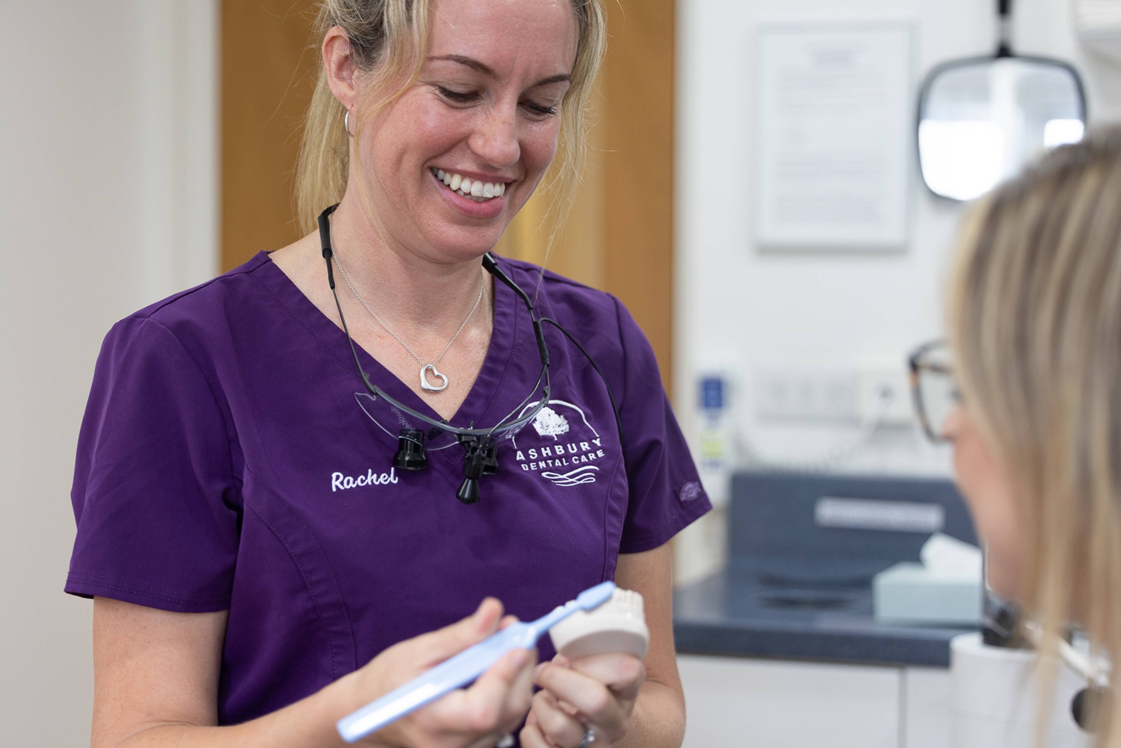 A hygienist demonstrates proper bushing technique using a toothbrush and an anatomic model of some teeth