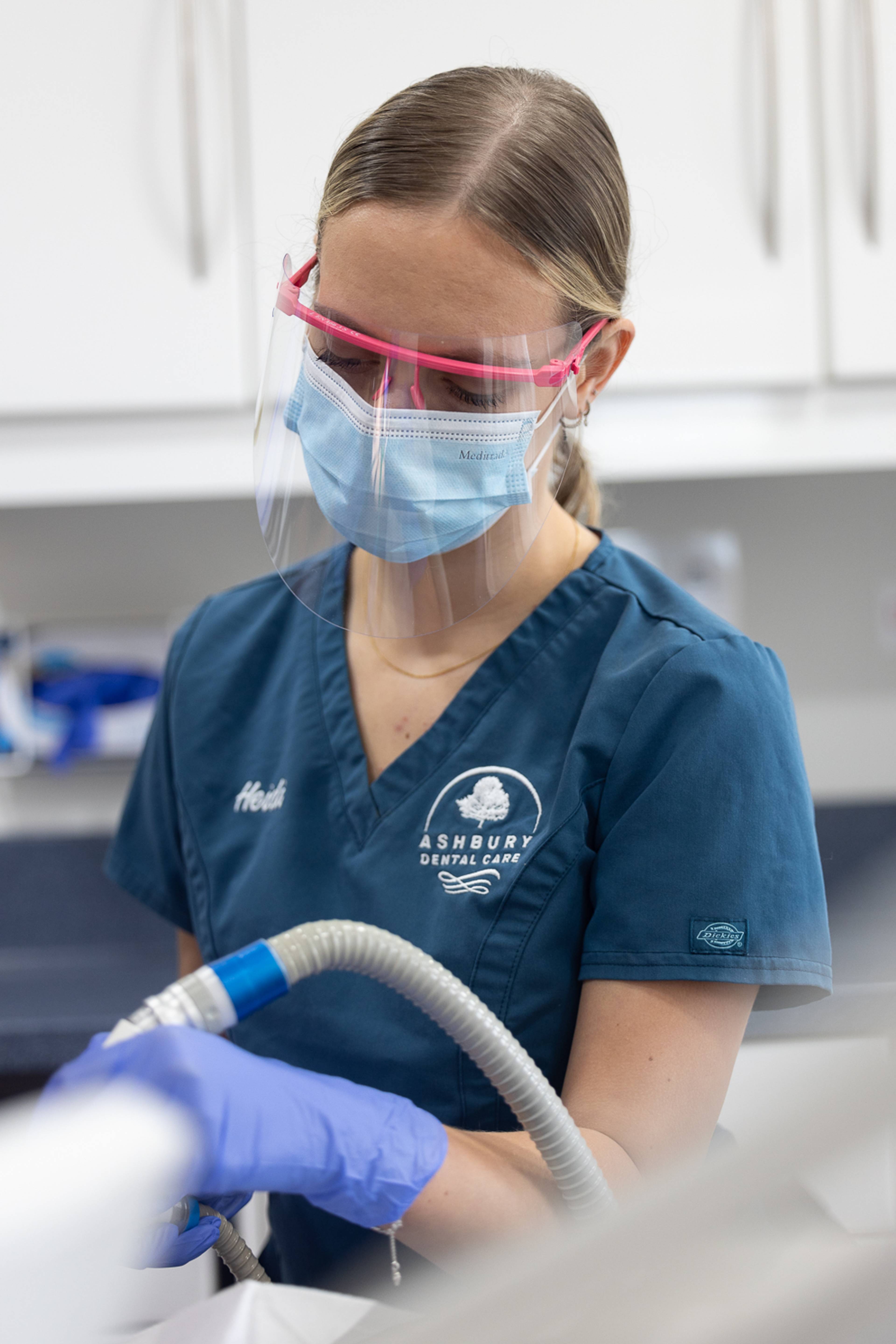 A patient with a face mask and dental loupes looking down at a patient who is out of frame