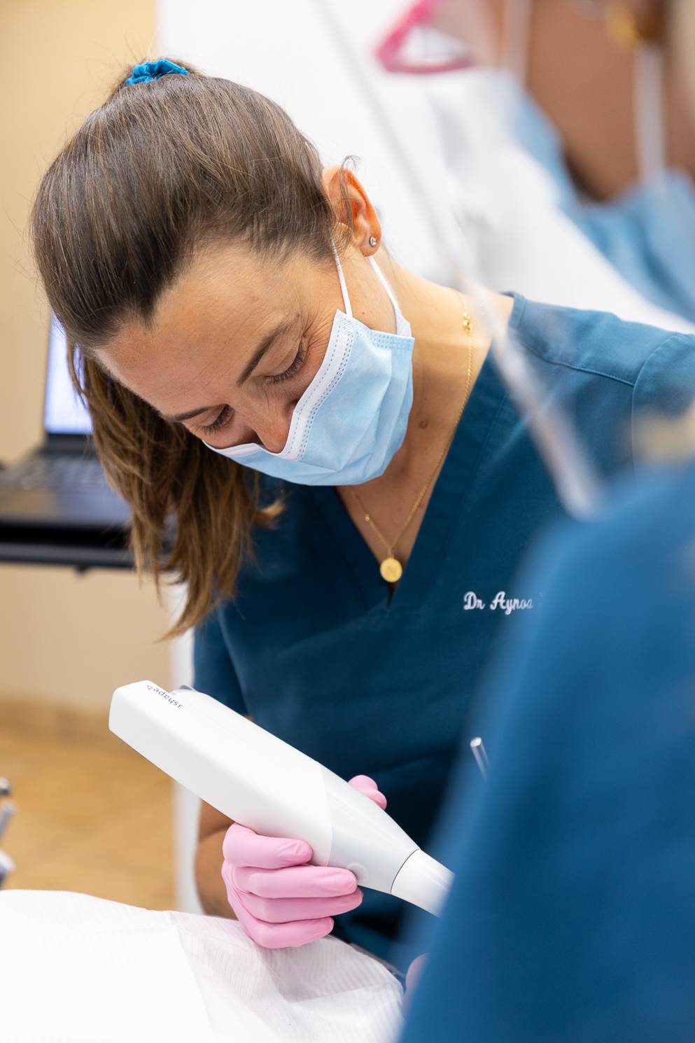A dentist wearing face mask looking down at a patient in the chair out of frame during an intra-oral scan