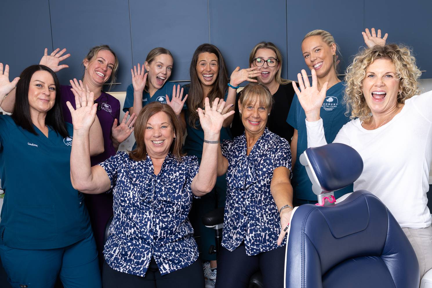 The whole dental team in a treatment room putting their hands in the air and smiling happily