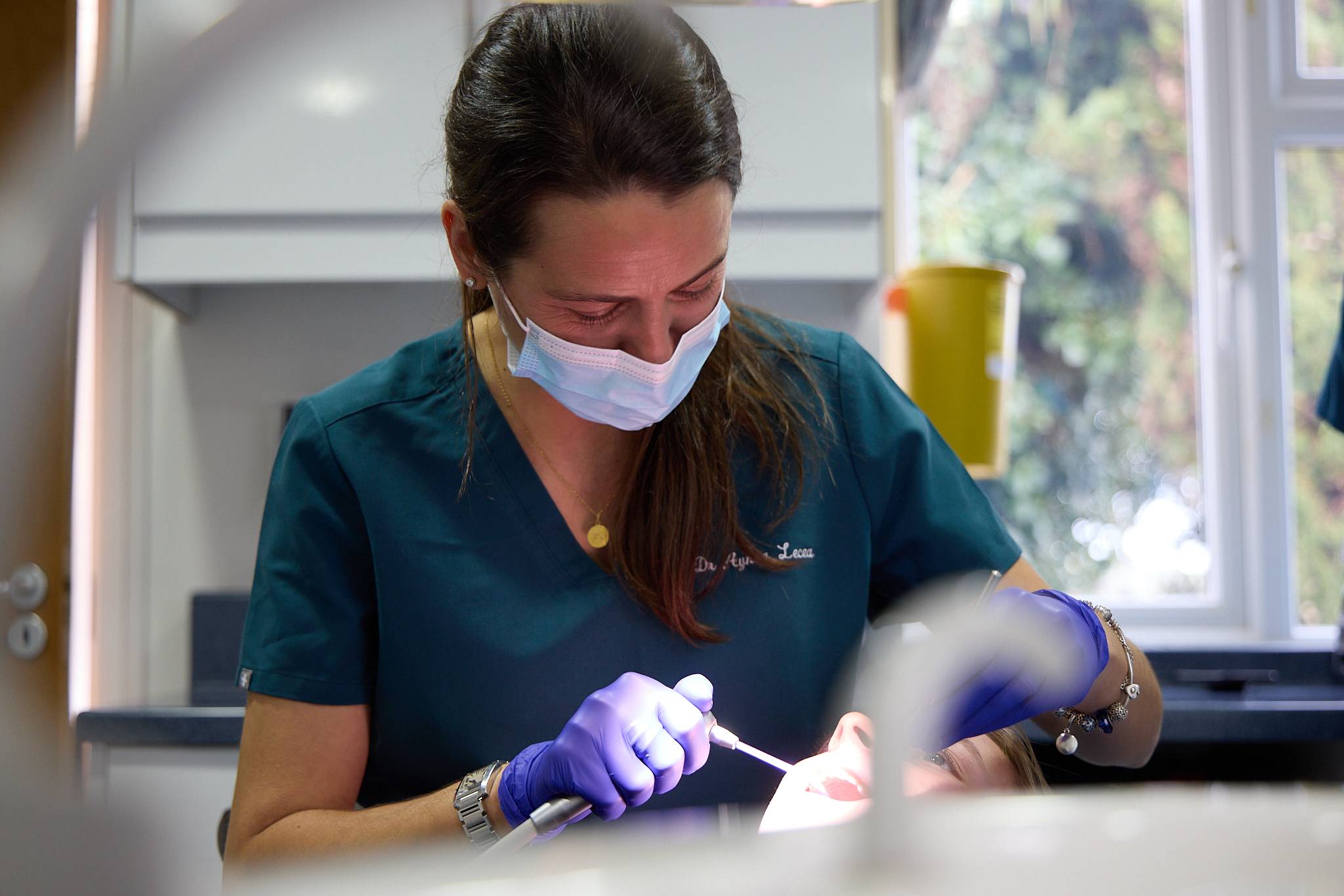 Dentist wearing a mask whilst looking down and treating patient out of frame