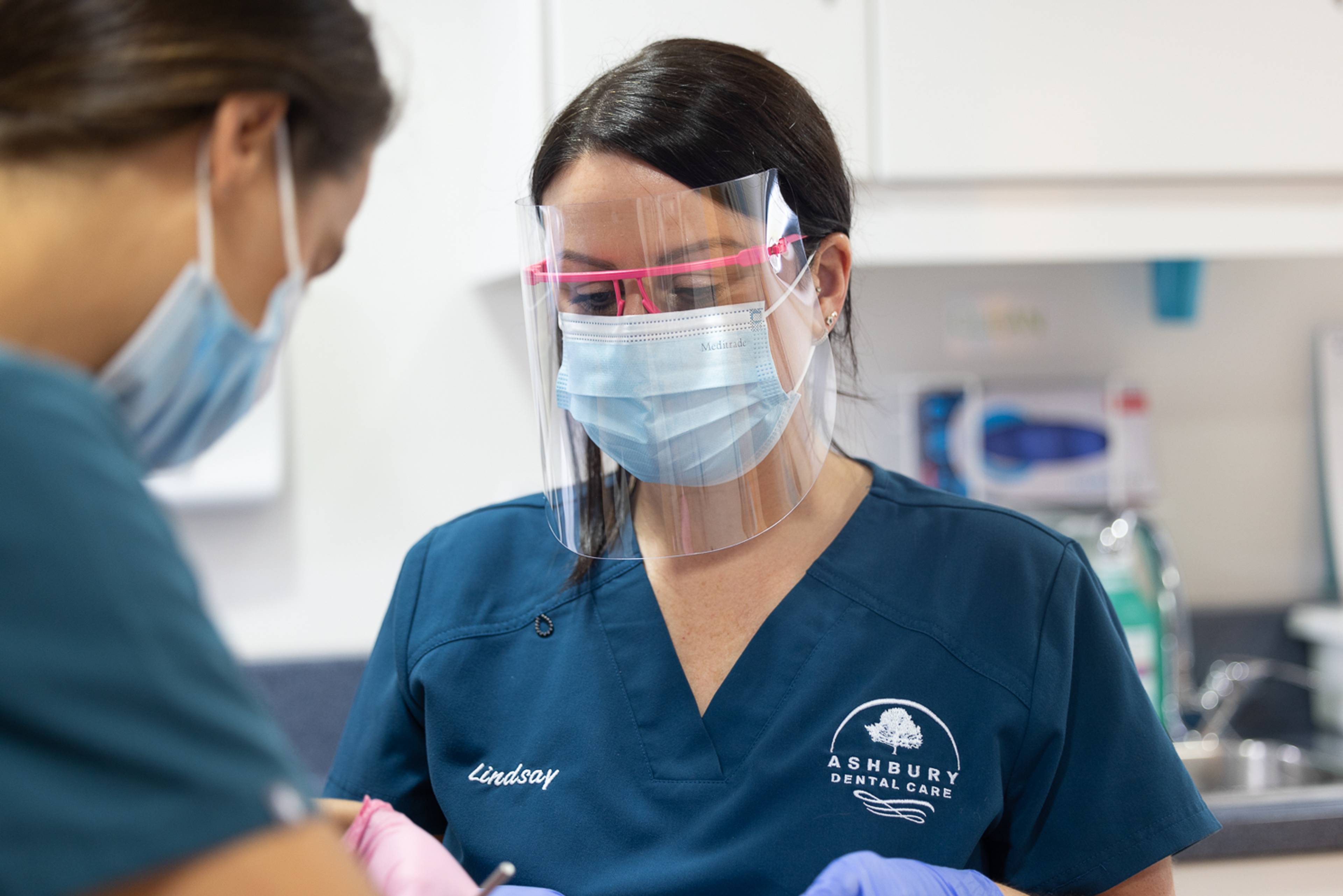 Two dentists in a treatment room wearing face masks and eye protection