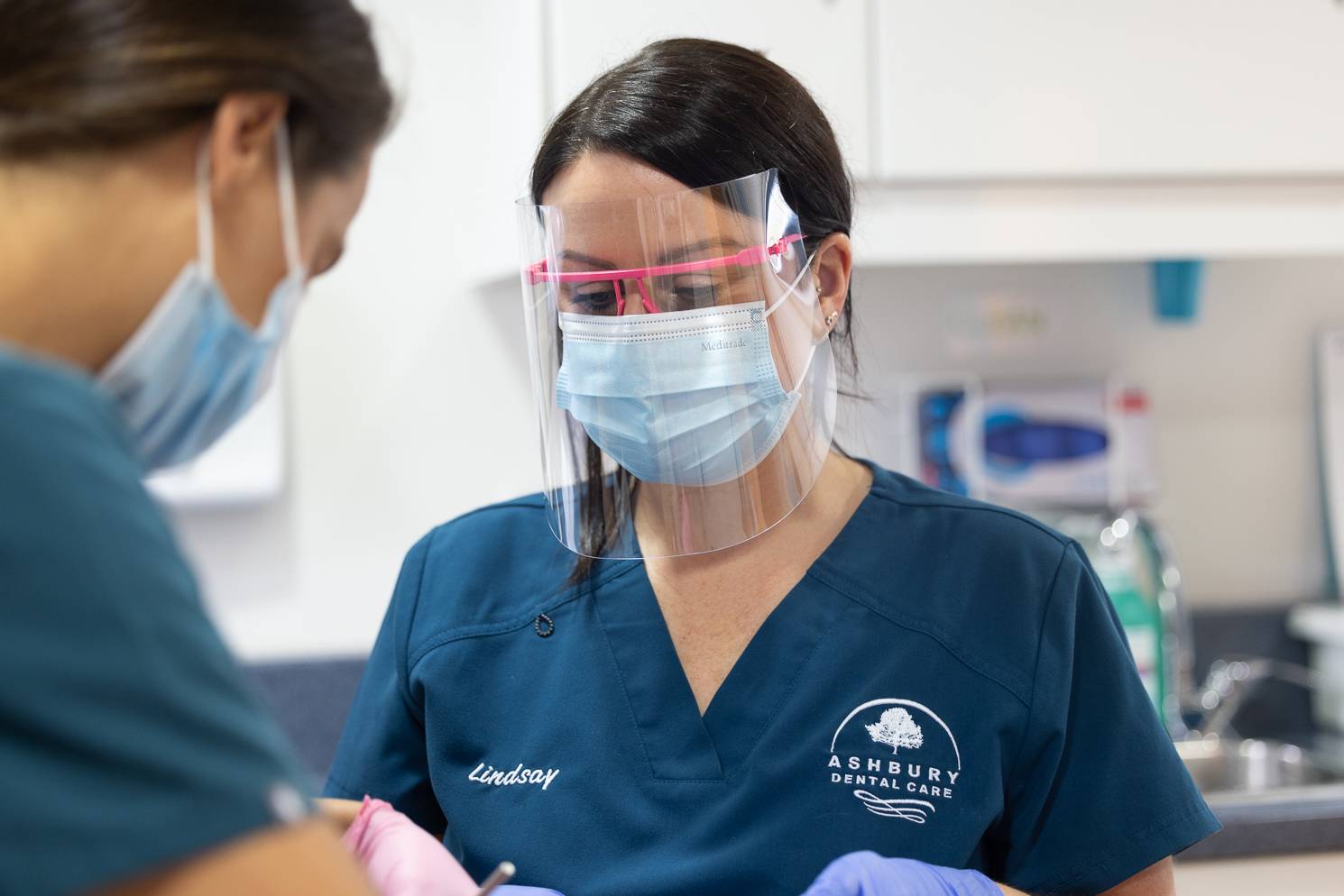 Two dentists in a treatment room wearing face masks and eye protection