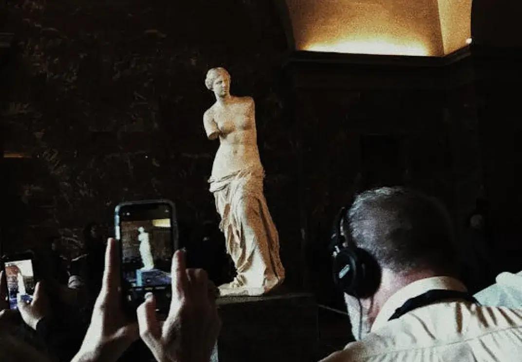 Visitors photographing the Venus de Milo statue in a museum
