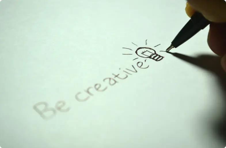 Handschrift "Sei kreativ" mit einer Glühbirnen-Skizze auf weißem Papier