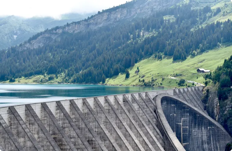 Represa de concreto en un paisaje montañoso con bosque y lago turquesa