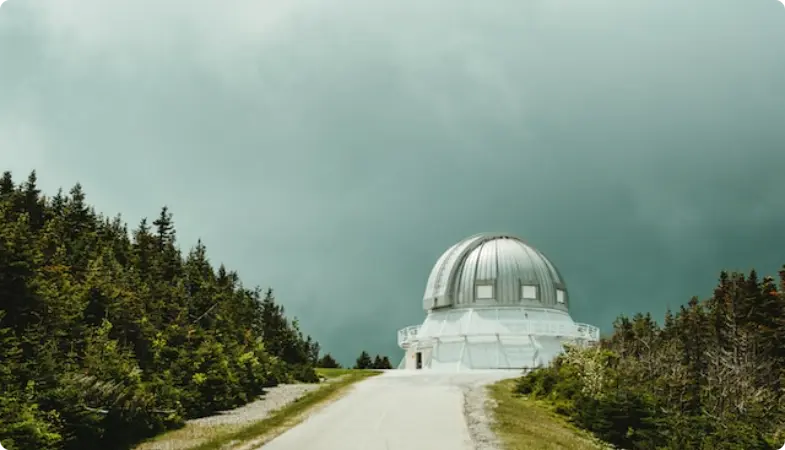 Cúpula blanca del observatorio anidada entre pinos bajo un cielo tormentoso