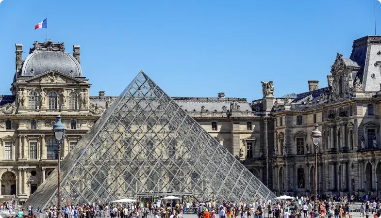 Glaspyramide ved Louvre Museum med historiske paladsbygninger og besøgende