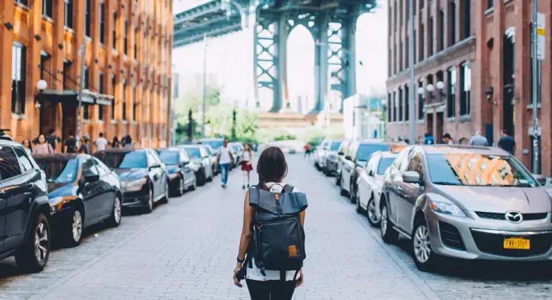 Person med rygsæk, der går ned ad en gade i Brooklyn med Manhattan Bridge i baggrunden