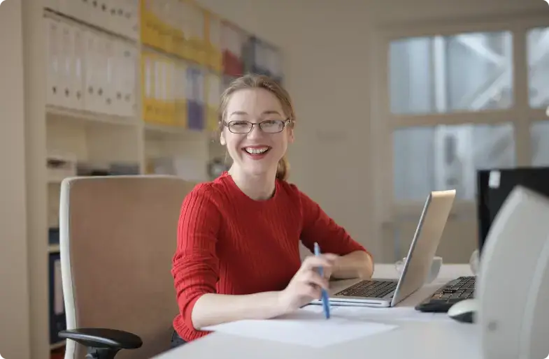 Professionnel souriant en pull rouge travaillant à un bureau avec un ordinateur portable et des papiers