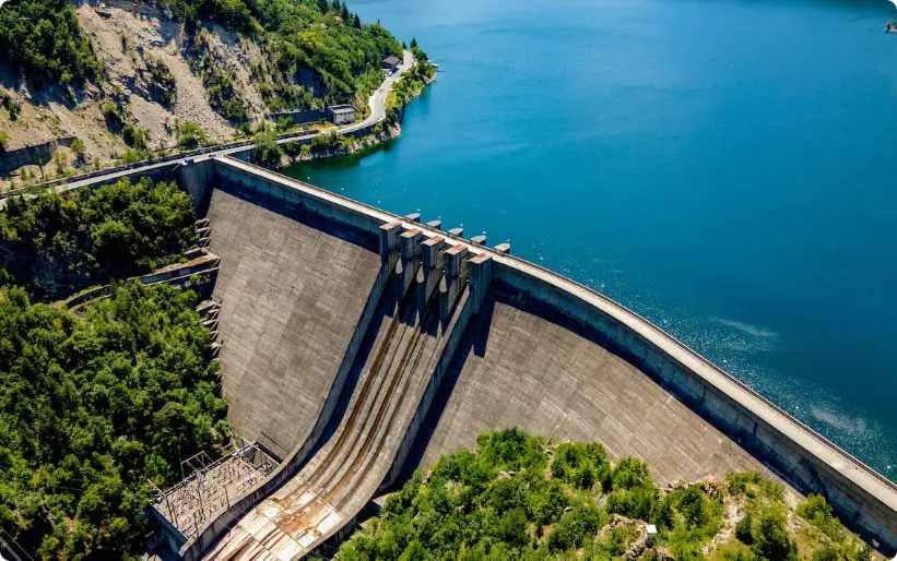 Grand barrage hydroélectrique en béton courbant à travers un lac bleu entouré de forêt