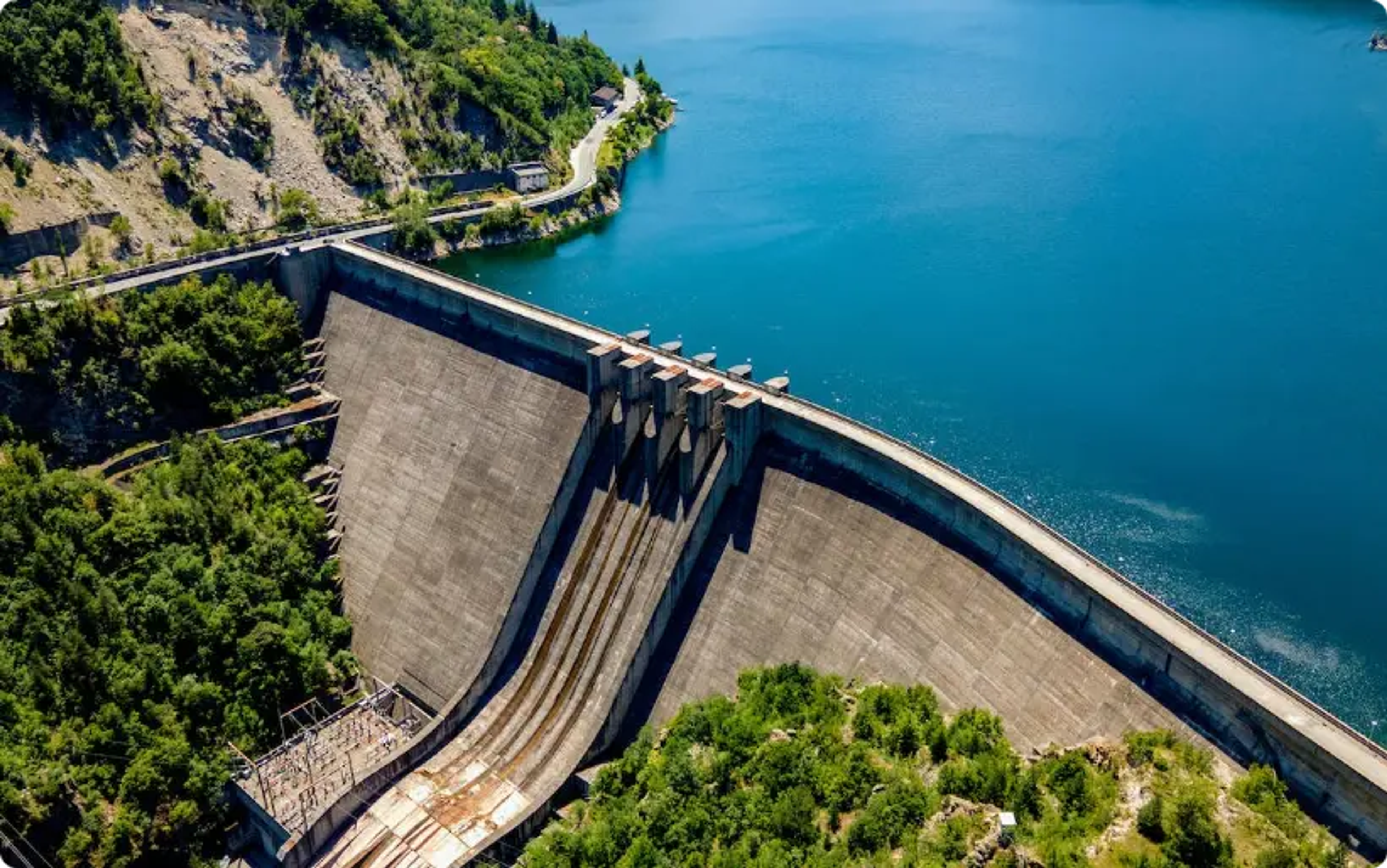 Grande barragem hidrelétrica de concreto curvando-se ao redor de um lago azul cercado por floresta