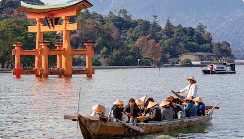 Pomarańczowa brama torii w wodzie z łodzią turystów w pobliżu wyspy Miyajima, Japonia