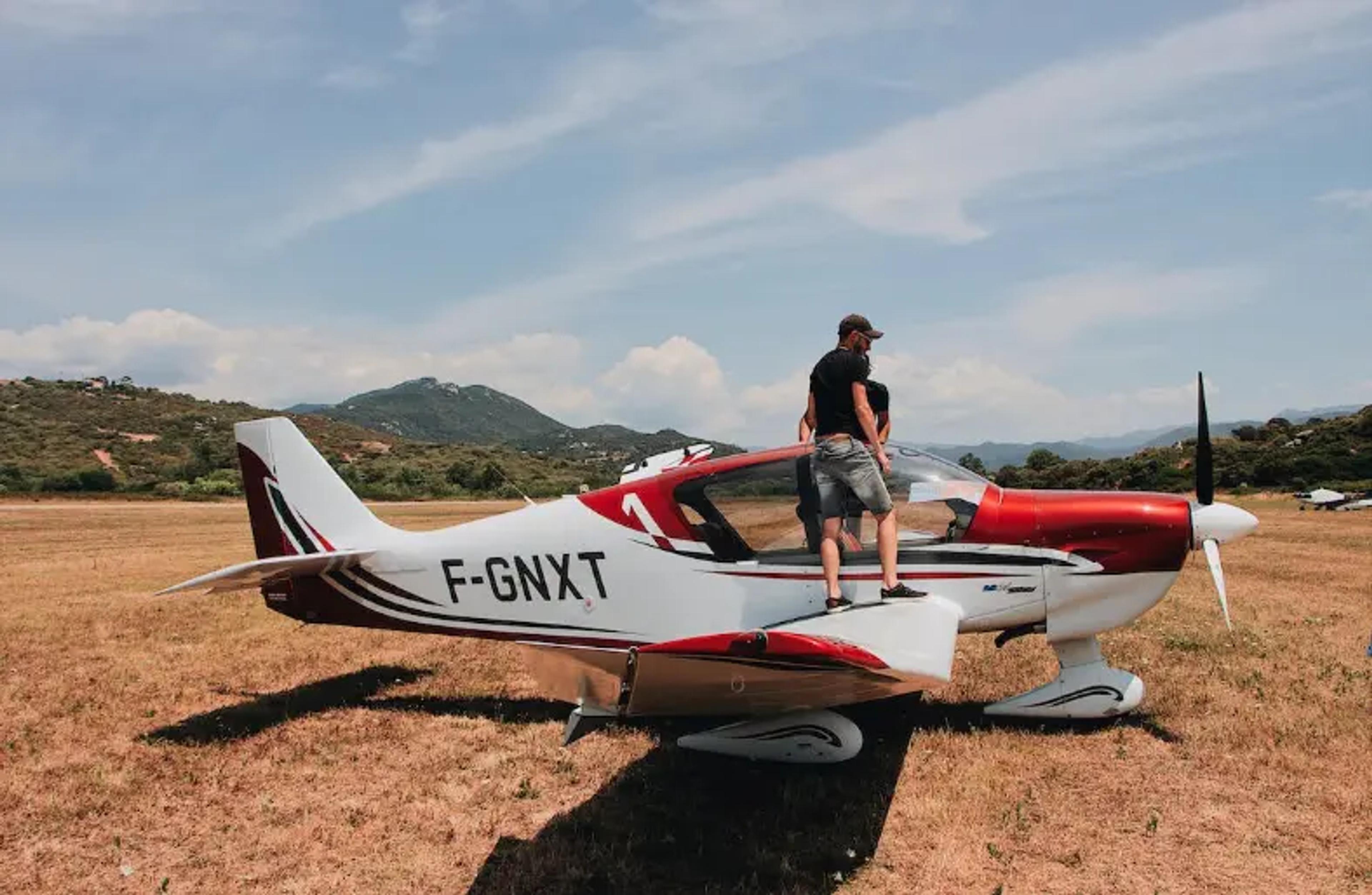Kleines rotes und weißes Flugzeug, das auf einem trockenen Feld mit Bergen im Hintergrund geparkt ist
