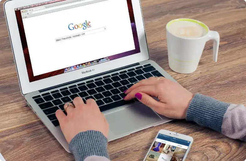 Person bruger MacBook med Google-søgning og kaffe på træbord